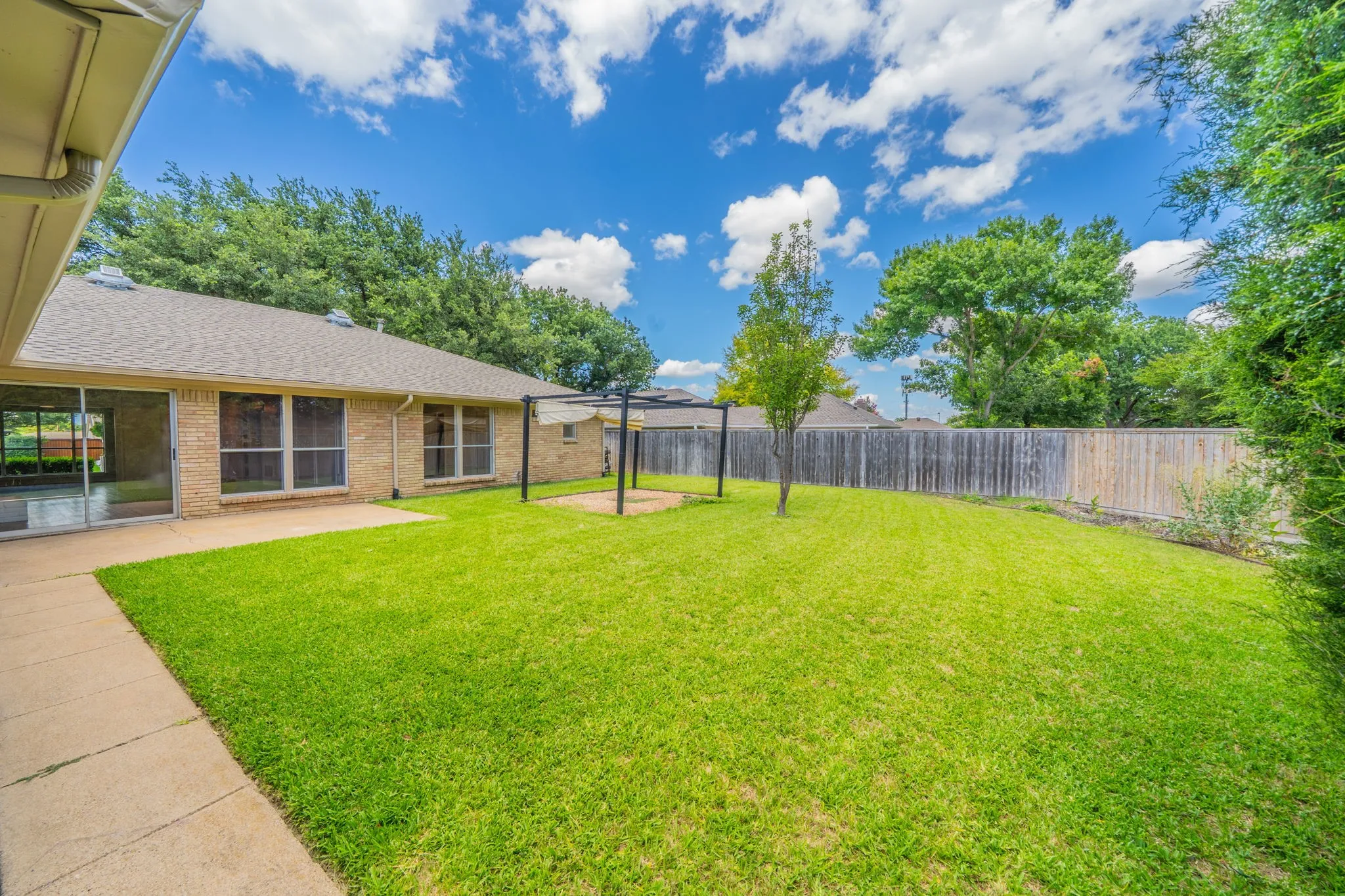 Spacious backyard featuring a lush lawn, concrete patio, and a privacy fence