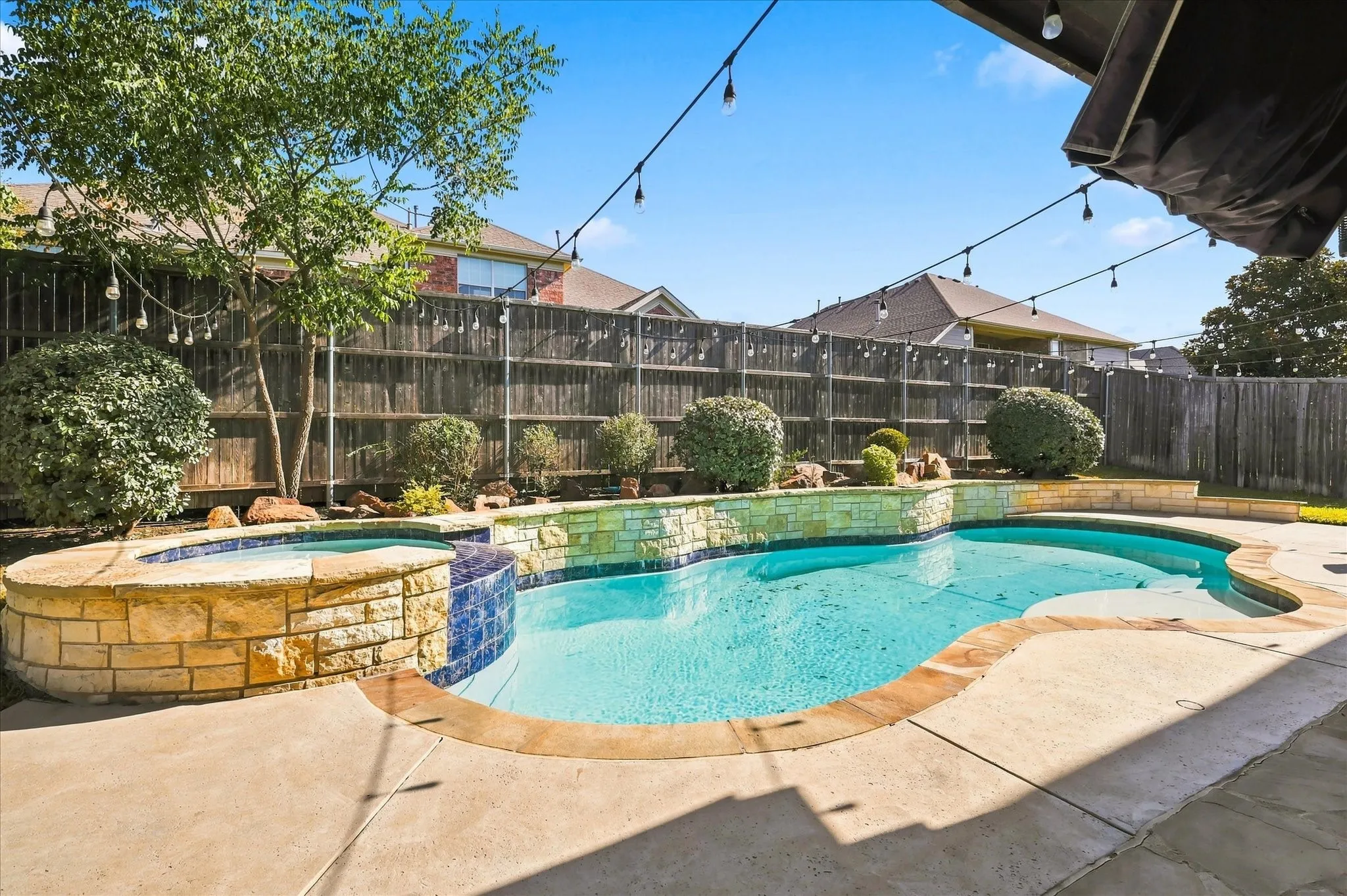 Outdoor swimming pool with integrated spa, stone-clad pool surround, concrete patio, and privacy fencing