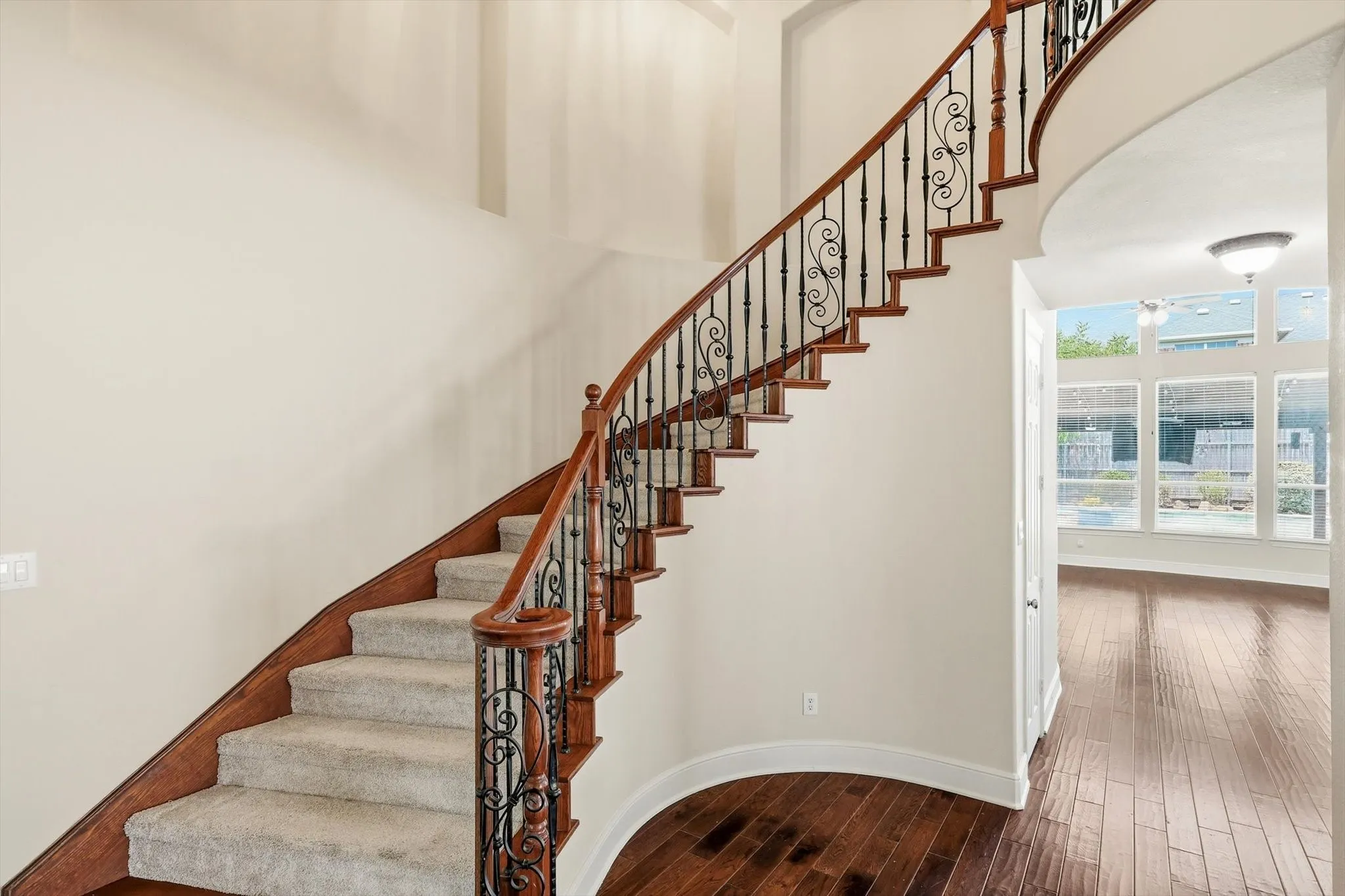 Curved staircase with wood-finish treads, carpeted risers, and ornate metal balusters