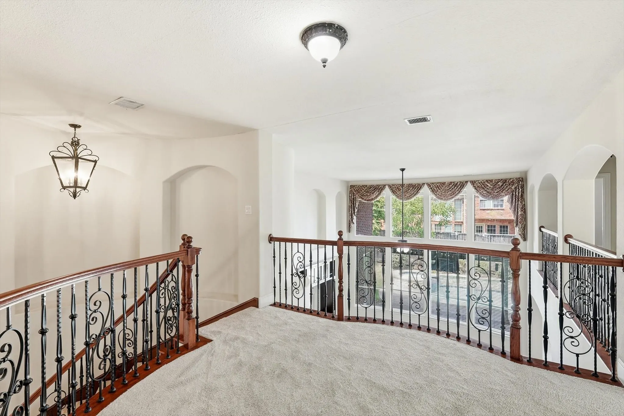 Upper-level landing with wrought iron and wood-finish railings, recessed archways, and a decorative pendant light fixture
