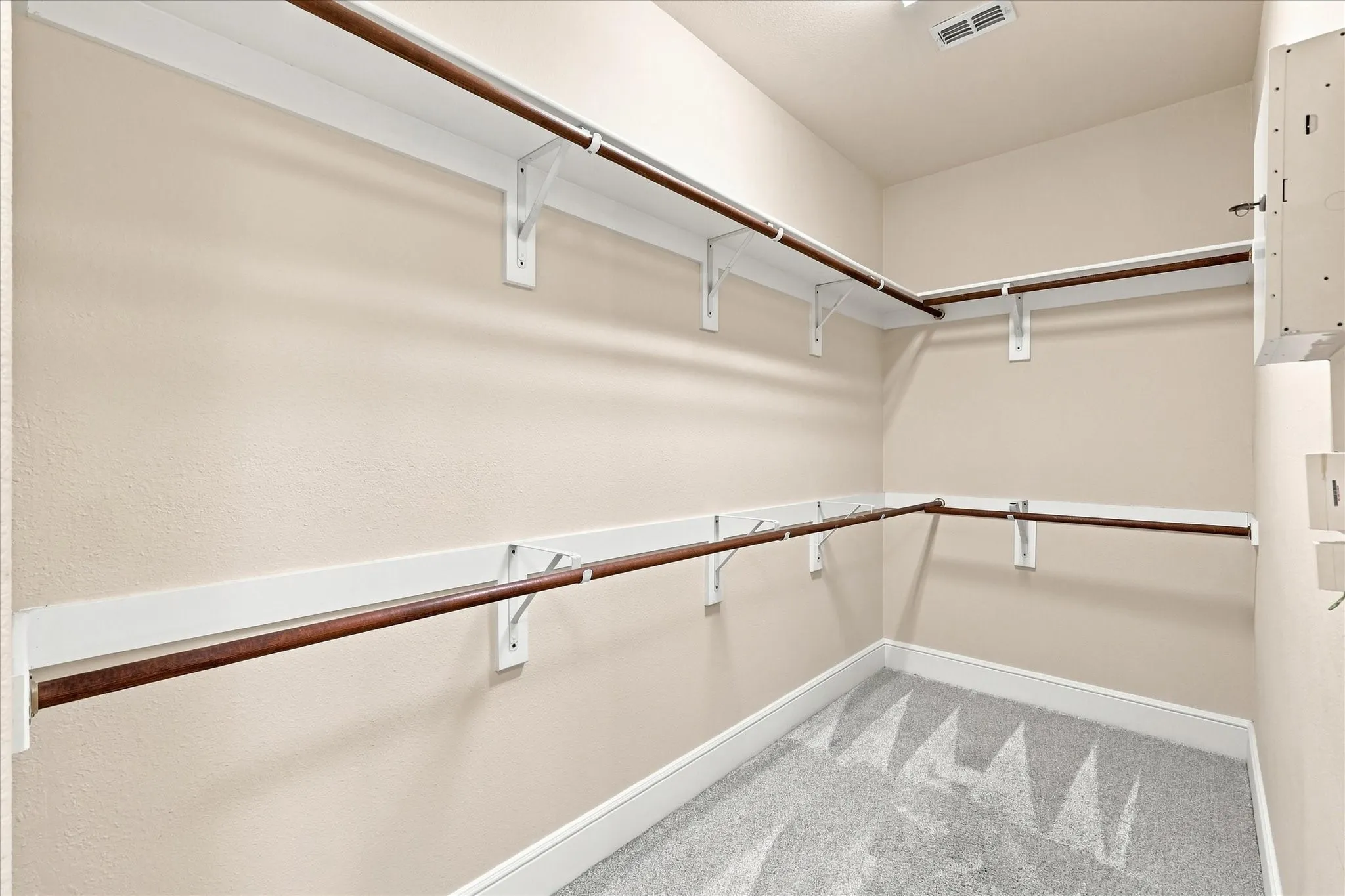 Walk-in closet with light-colored walls, white shelving, and wood-finish rods