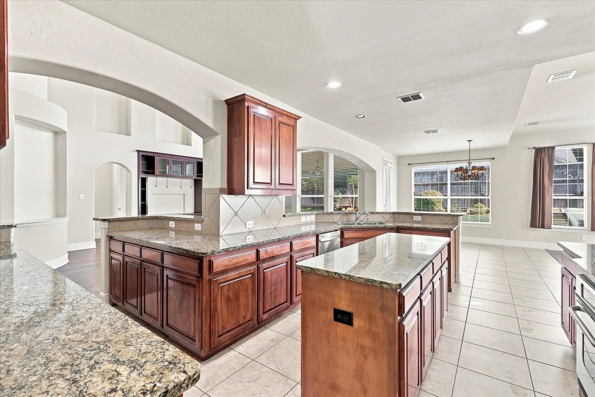 Expansive kitchen featuring granite countertops, wood cabinetry, tile flooring, recessed lighting, and a tile backsplash