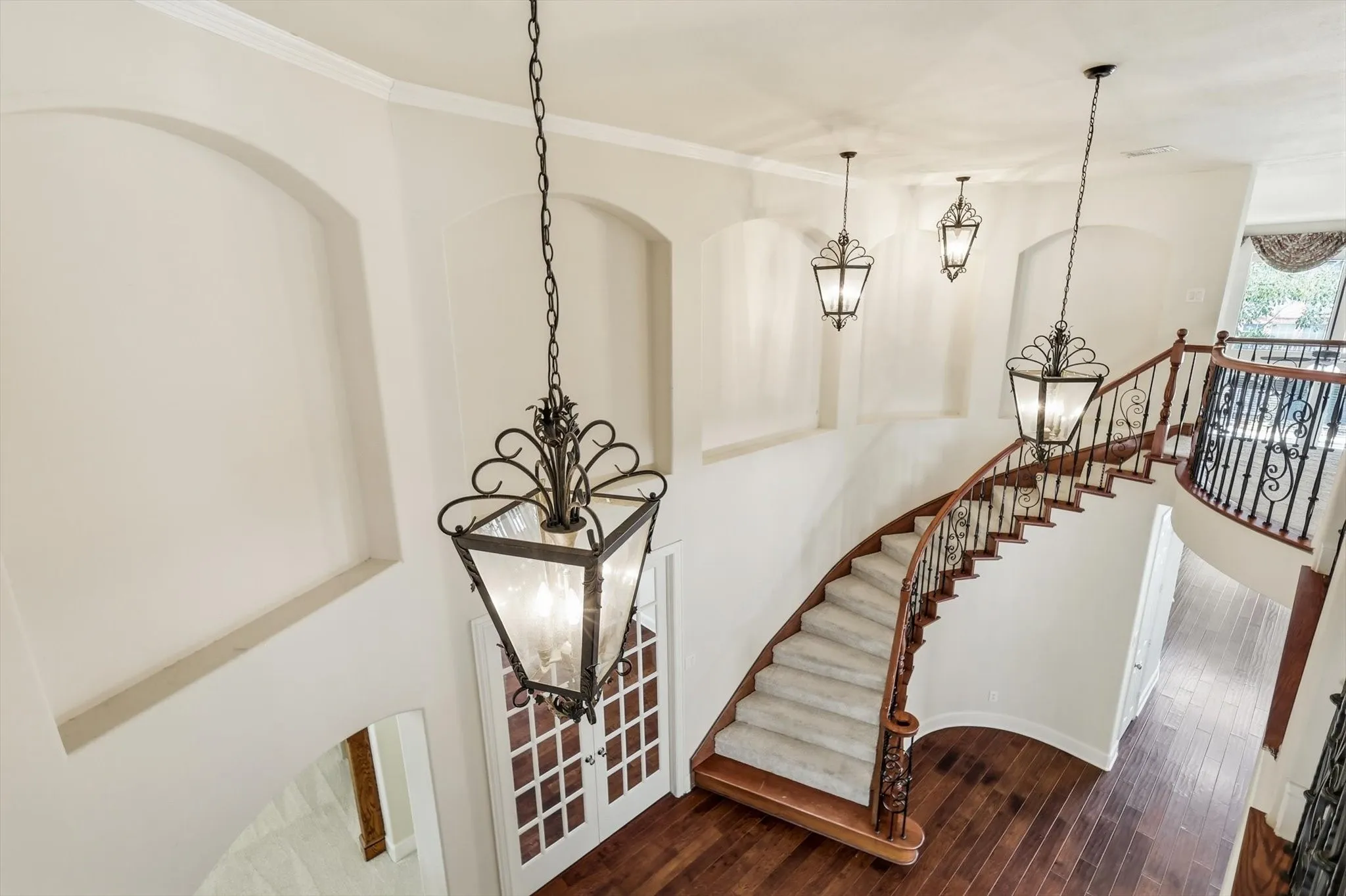 Grand curved staircase featuring wood-finish flooring, wrought iron balusters, and overhead decorative lanterns