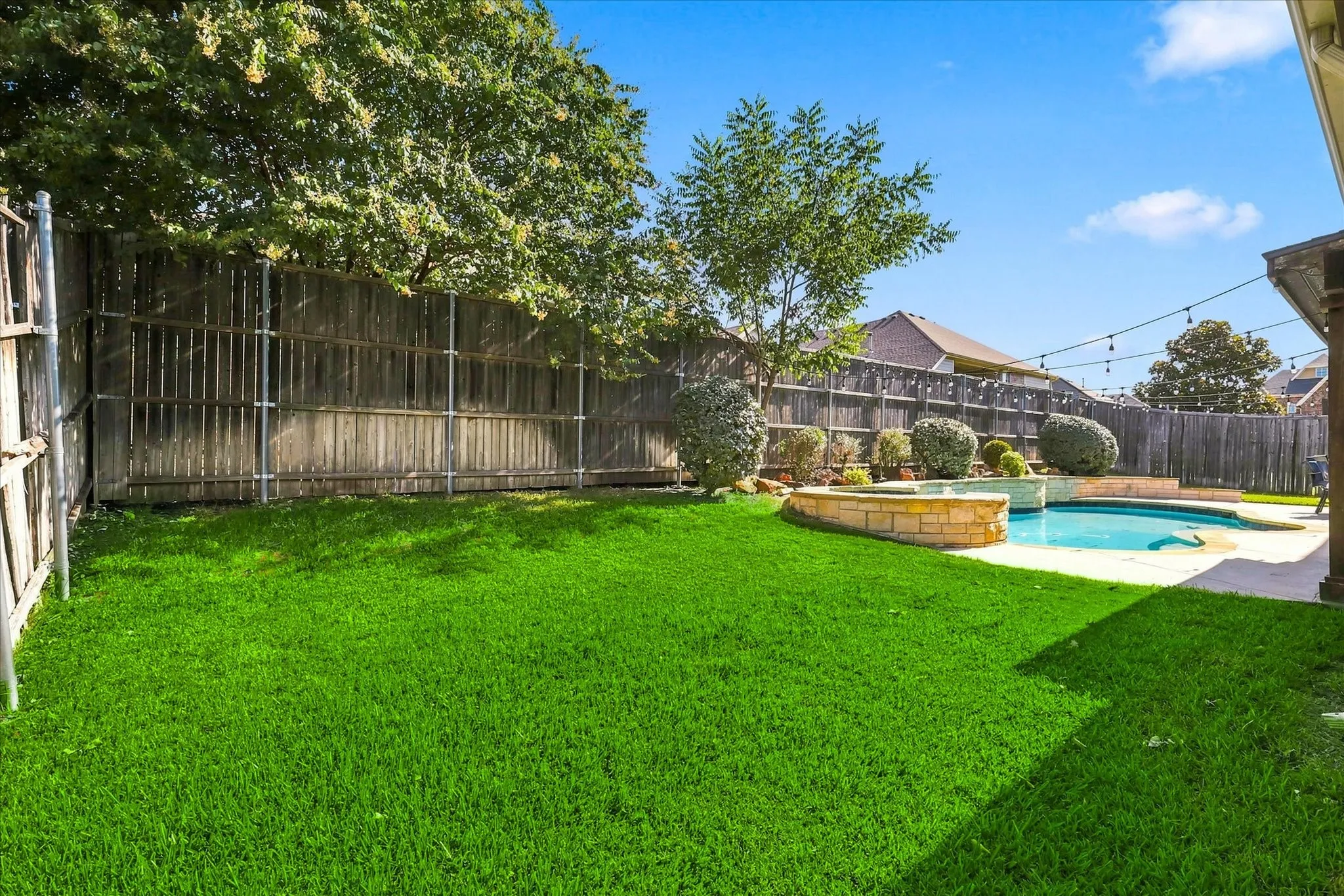 Expansive backyard featuring a manicured lawn, a swimming pool with integrated spa, a stone-accented perimeter, and mature landscaping