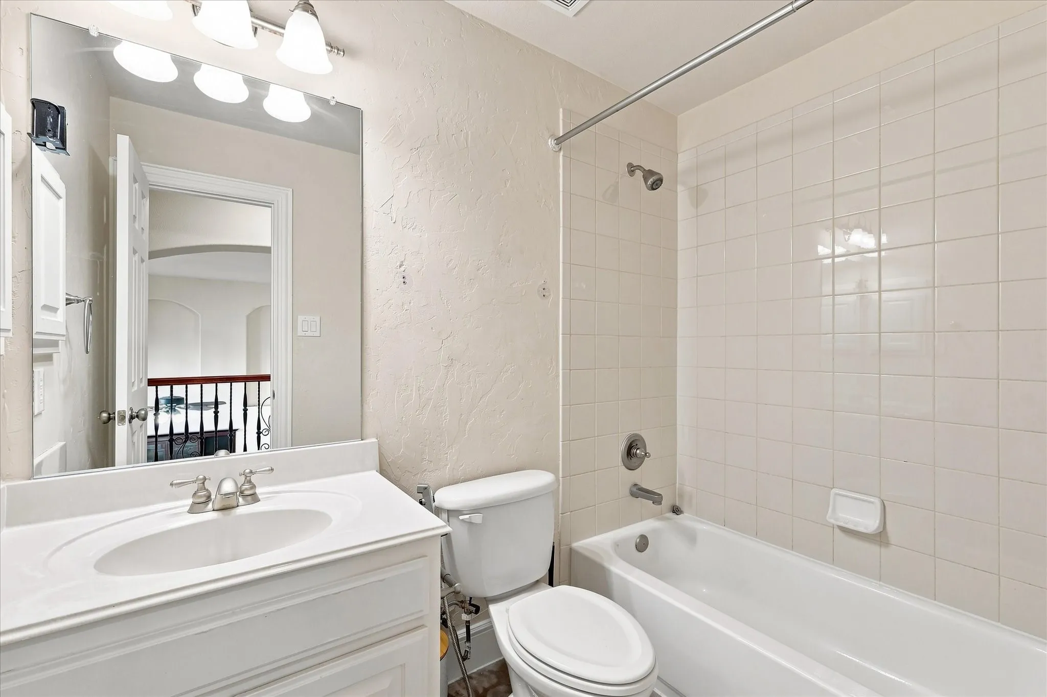 Bathroom featuring a vanity with an integrated sink, a three-bulb light fixture, a toilet, and a shower-bathtub combination with white tiled walls