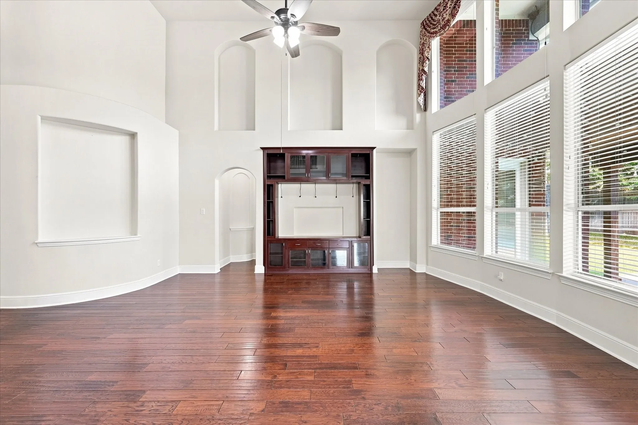 Wood-finish flooring, built-in entertainment center, high ceilings, large windows with blinds, and architectural wall niches