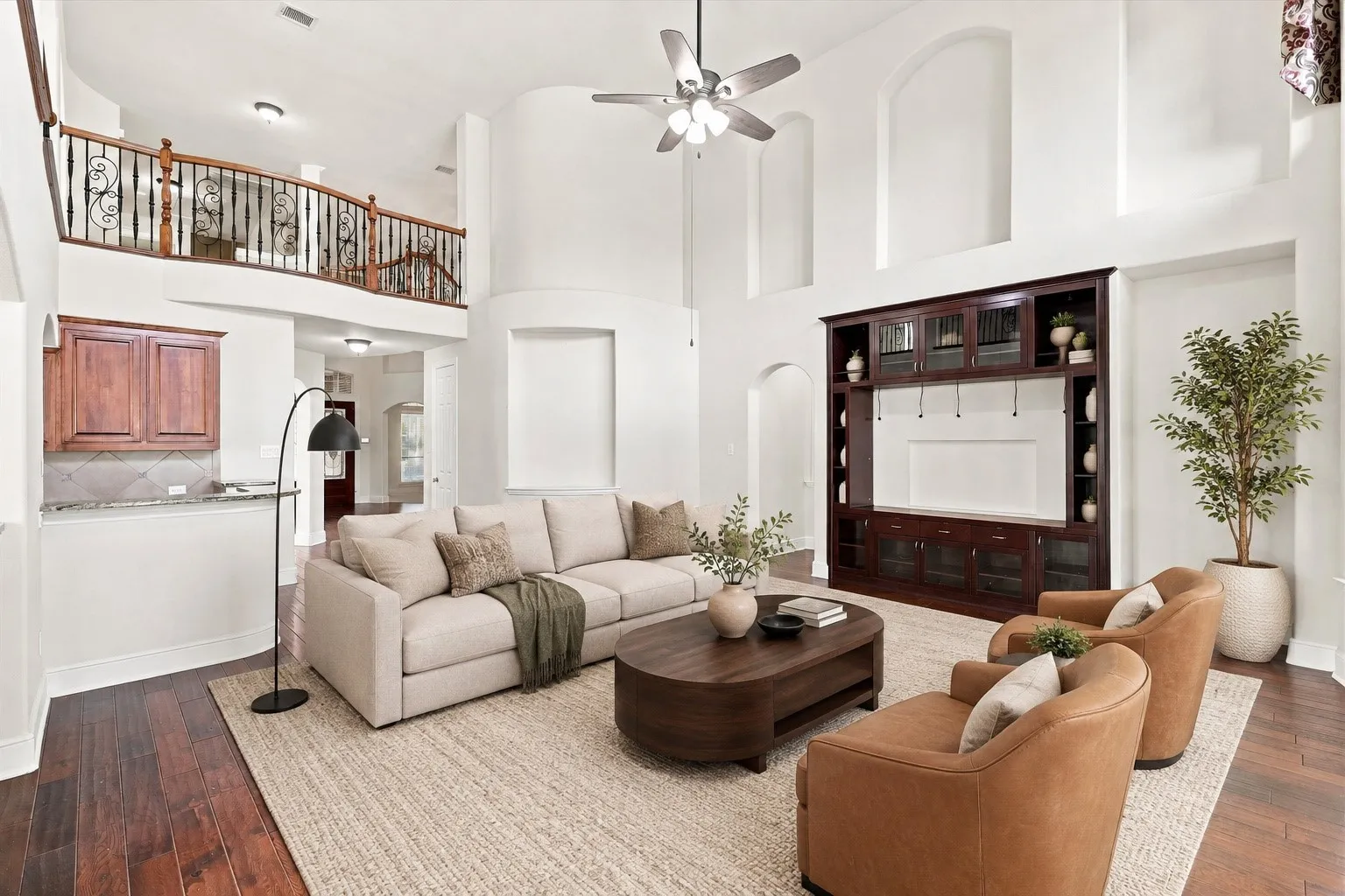 Virtually Staged Two-story living area with high ceilings, built-in media cabinetry, wood-finish flooring, and an upper-level balcony with wrought iron railing
