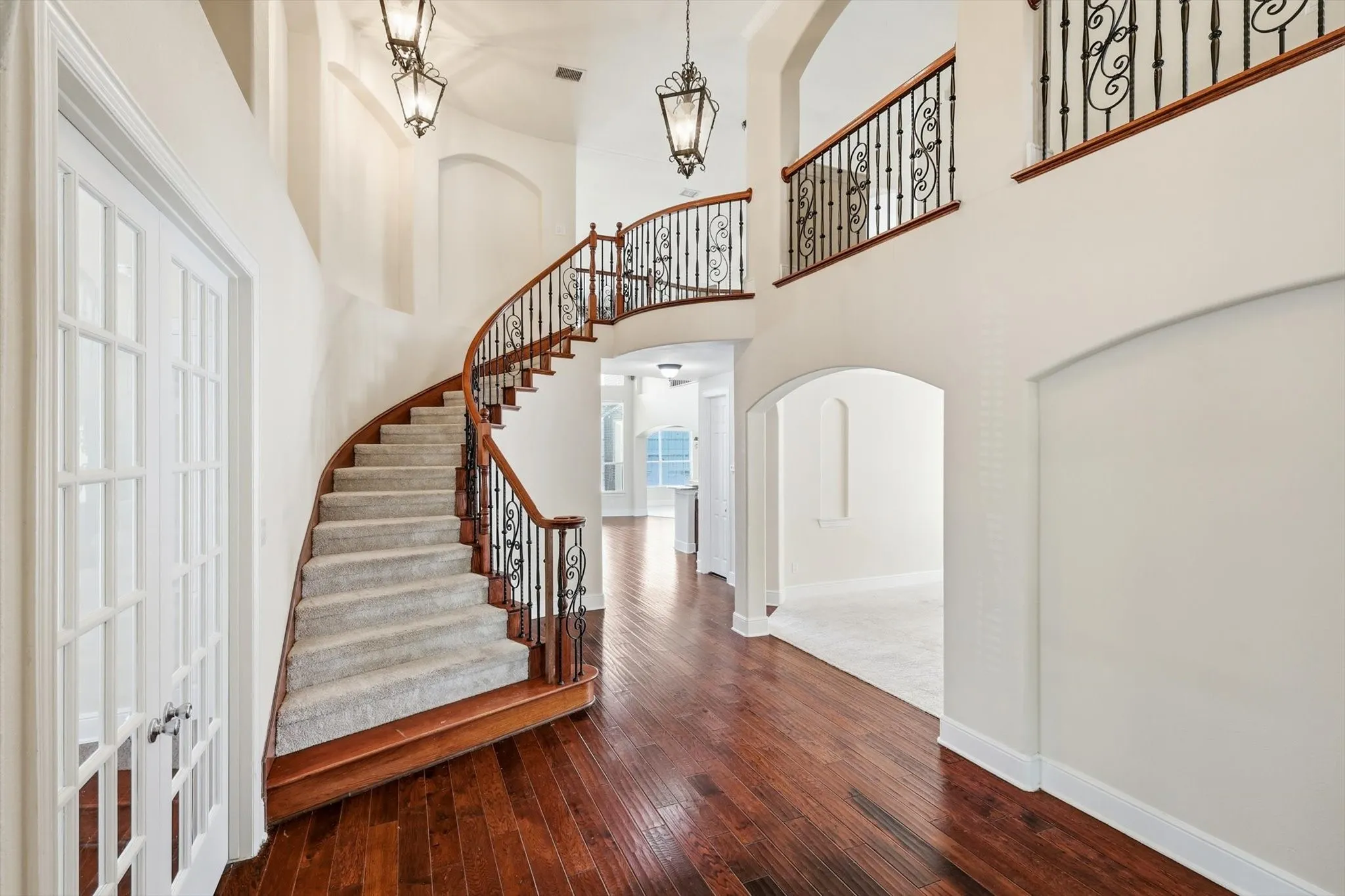 Grand foyer with wood-finish flooring and a curved staircase featuring wood banisters and wrought iron balusters