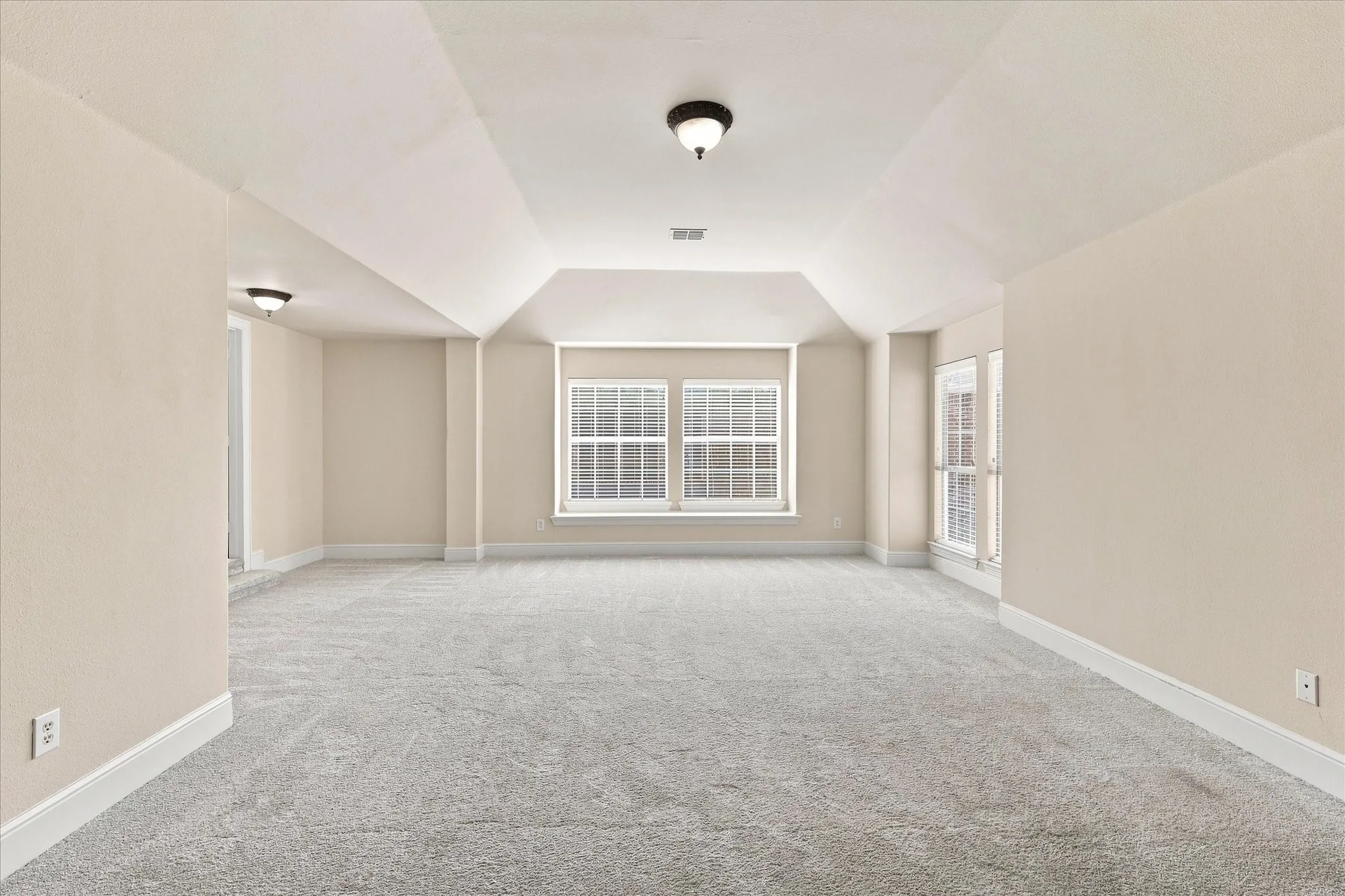 Expansive room featuring light-toned carpet, multiple windows, and a vaulted ceiling detail