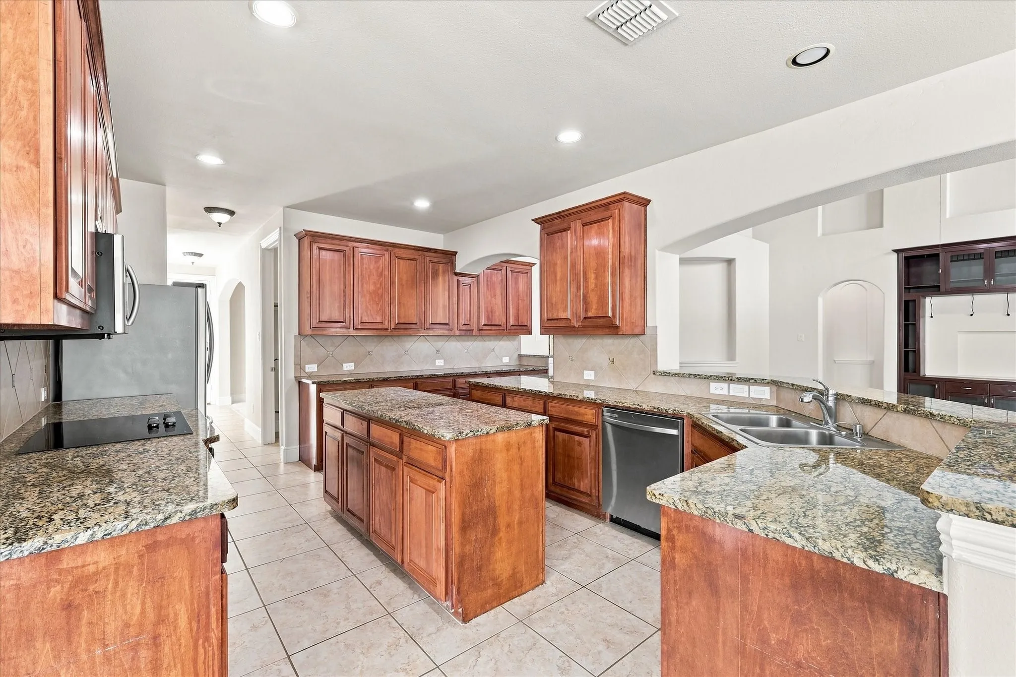Kitchen featuring a central island, granite countertops, tile flooring, wood cabinetry, and stainless steel appliances