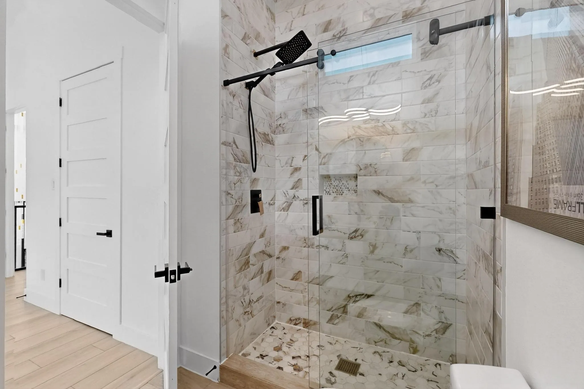 Glass-enclosed shower featuring marble-look subway tile, a built-in shower niche, and a contrasting mosaic tile floor