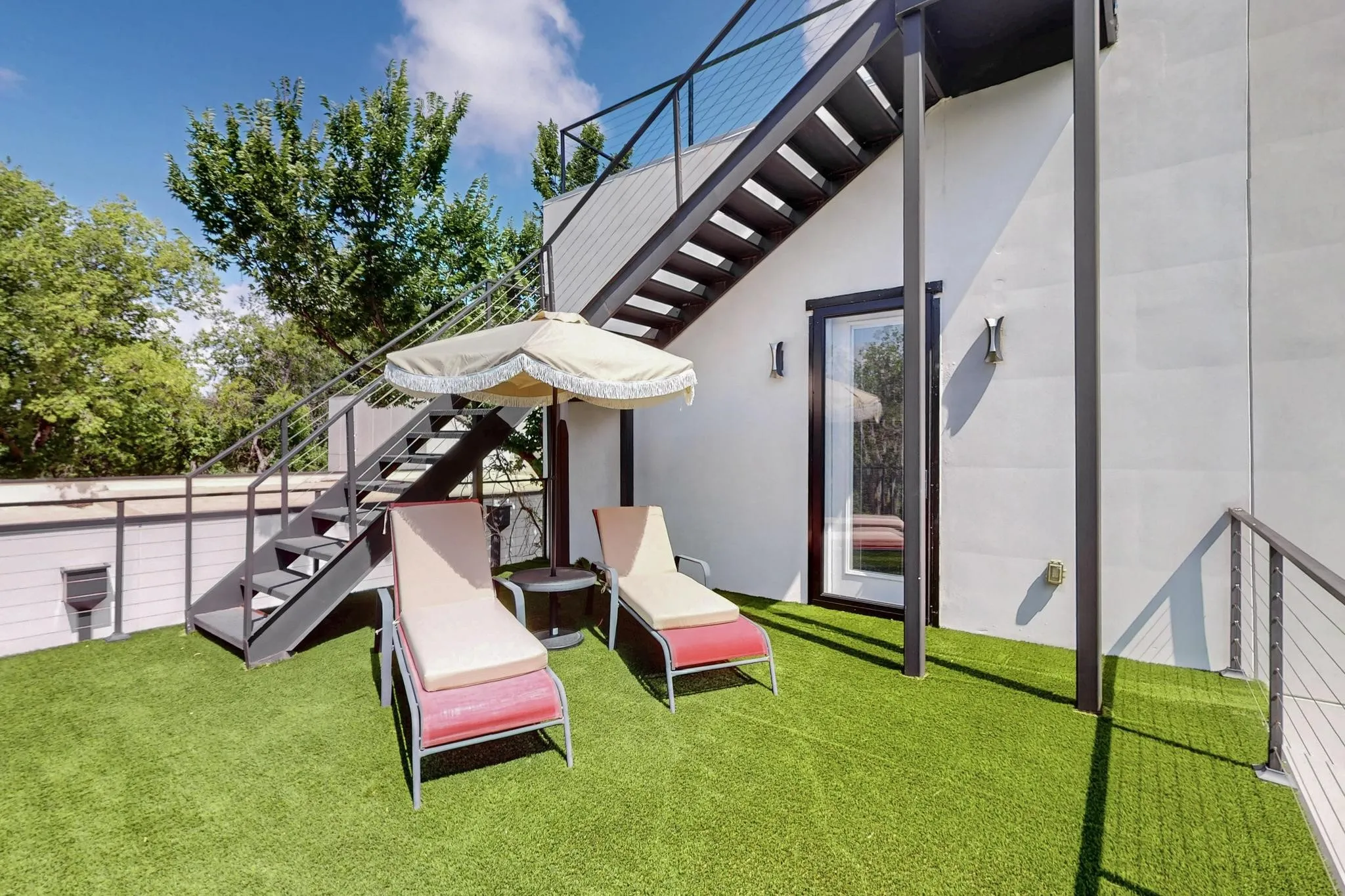 Rooftop deck featuring artificial turf flooring, a metal staircase with cable railings, and a glass-paneled exterior door