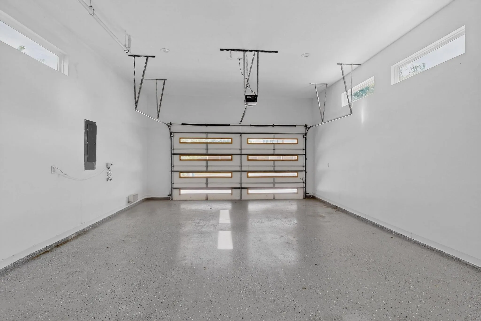 Spacious garage featuring a modern overhead door with frosted glass panels, durable epoxy flooring, crisp white walls, and high transom windows