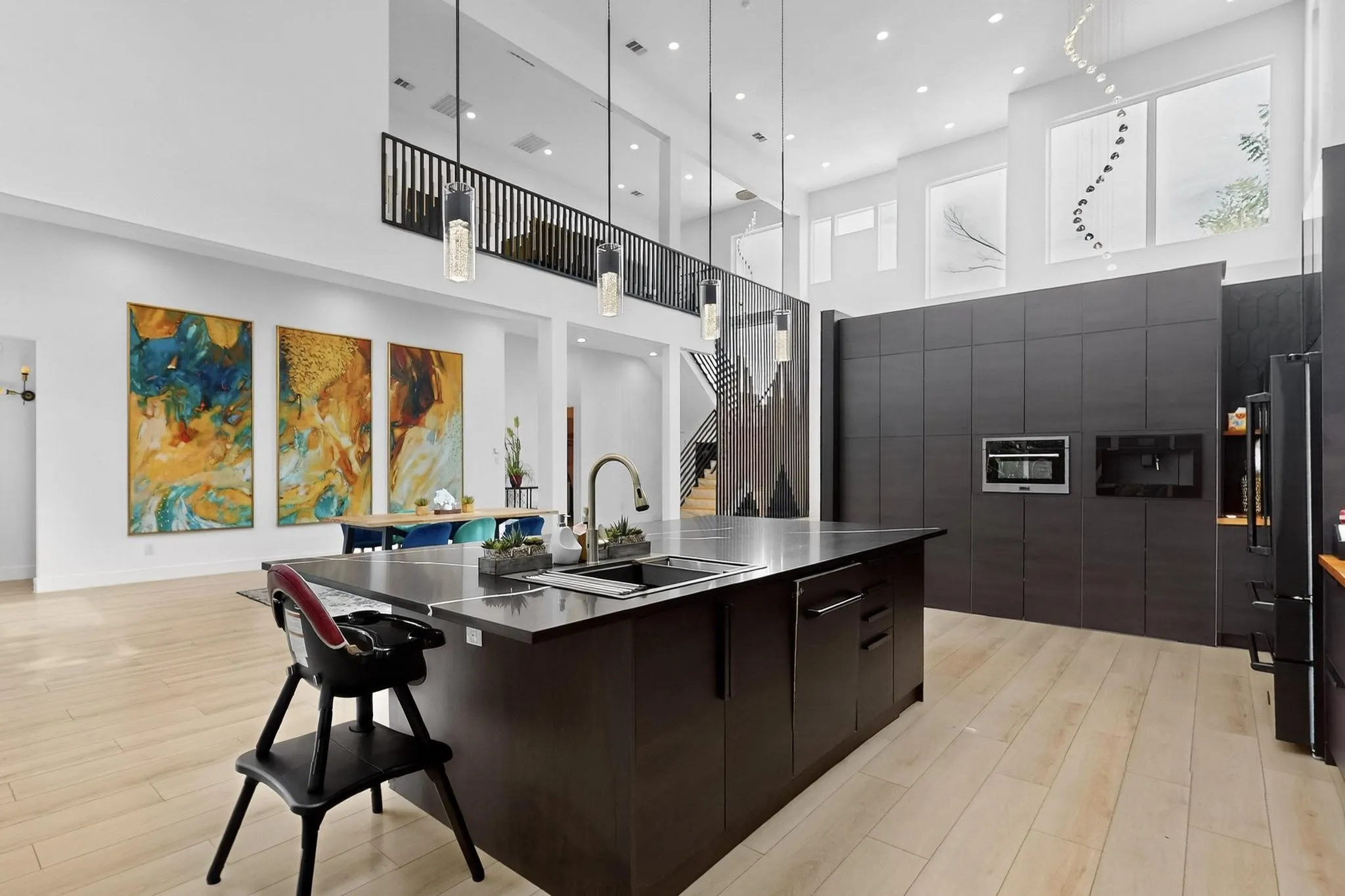 Modern kitchen featuring a large island with an undermount sink and dark countertop, integrated appliances, light wood-finish flooring, and high ceilings with upper-level windows