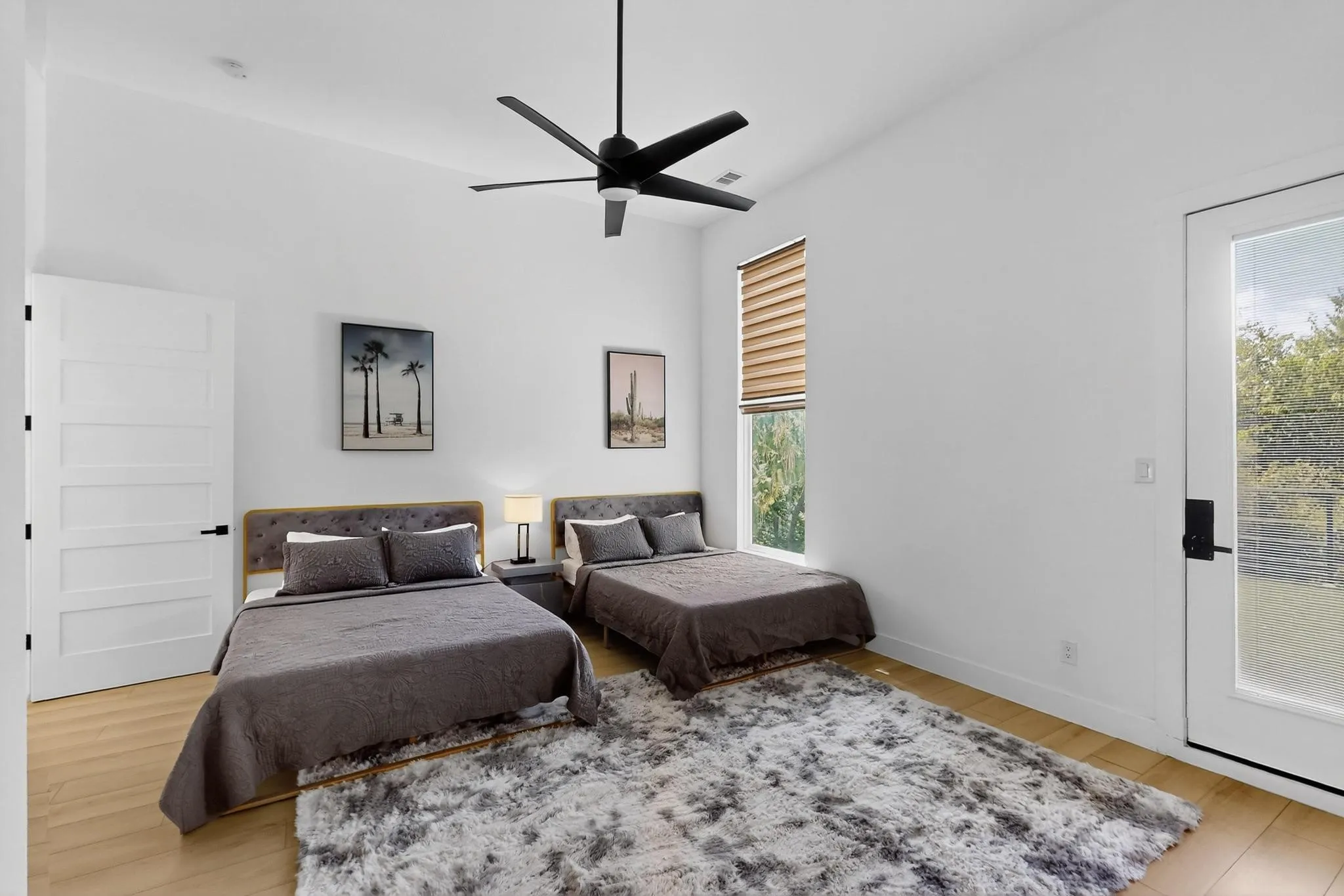 Spacious room featuring wood-finish flooring, high ceilings, a modern ceiling fan, and ample natural light from a large window with blinds and a glass-paneled door