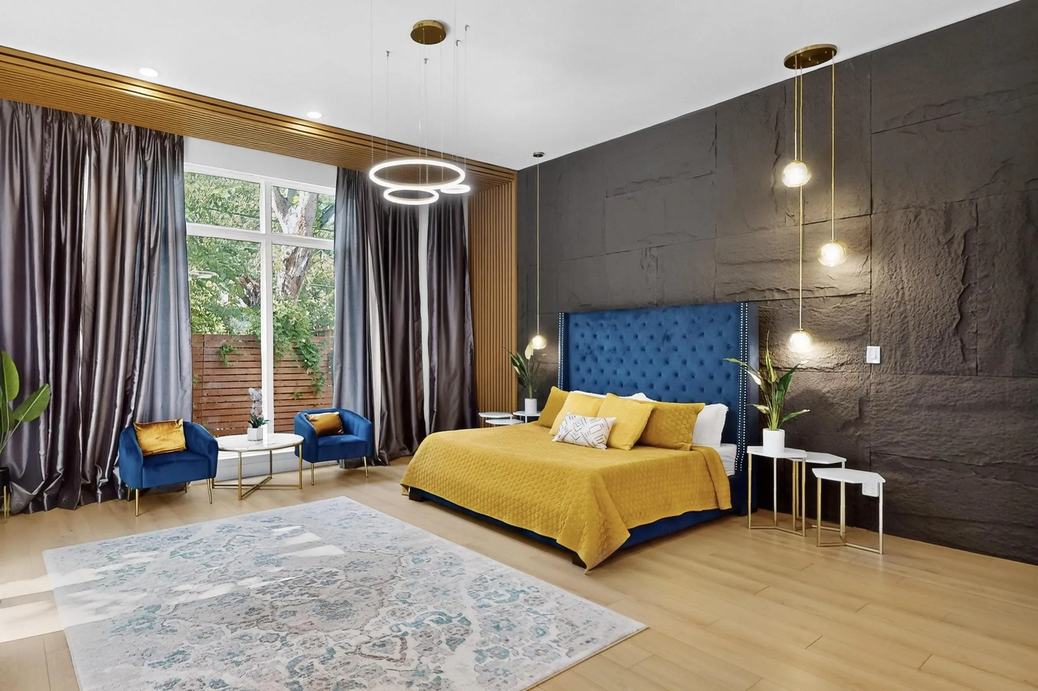 Spacious interior featuring a large window, light wood-finish flooring, a dark stone-textured accent wall, and contemporary pendant lighting fixtures