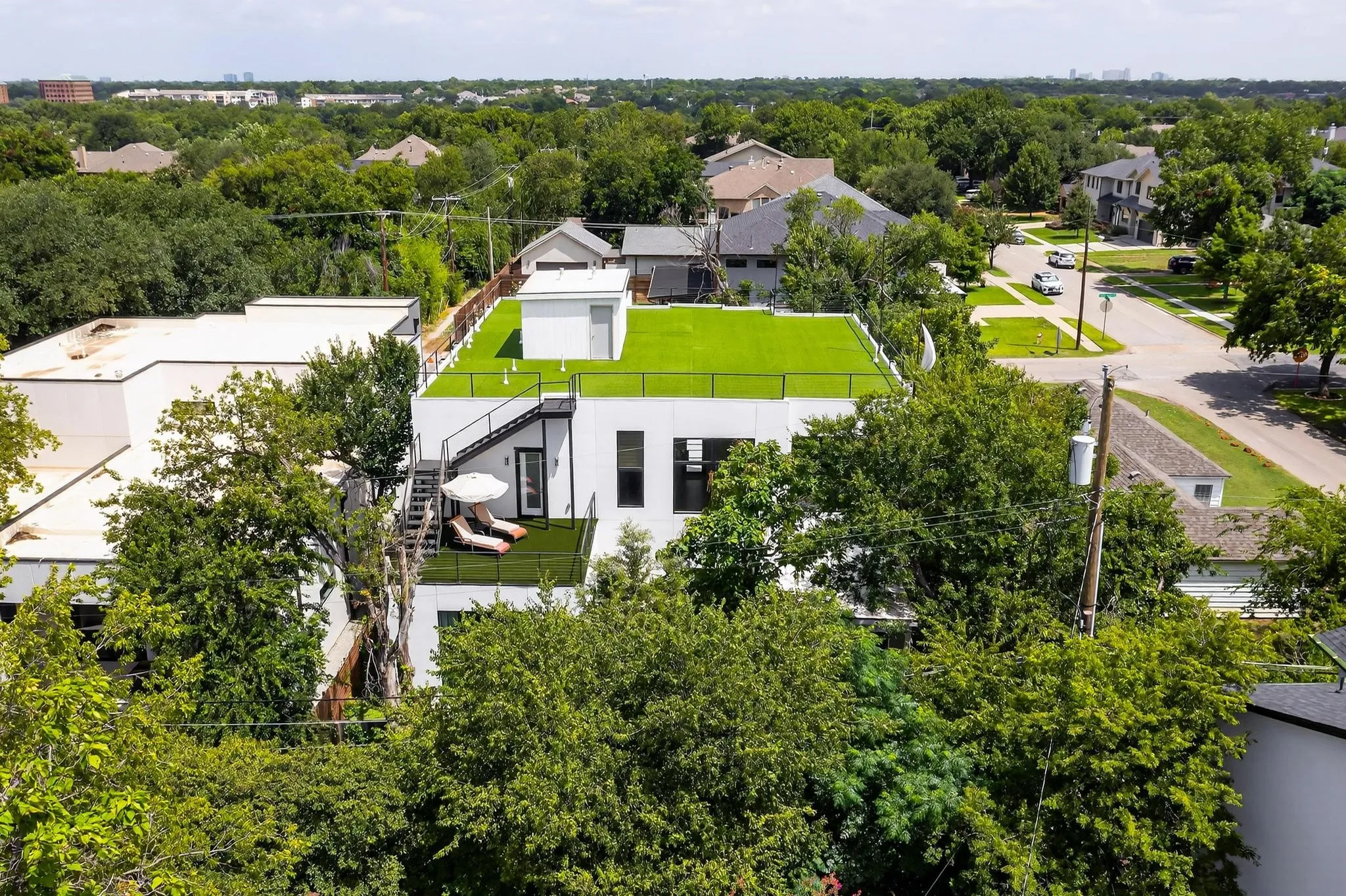 Modern architecture featuring a rooftop terrace with artificial turf, an exterior staircase, and an upper-level balcony