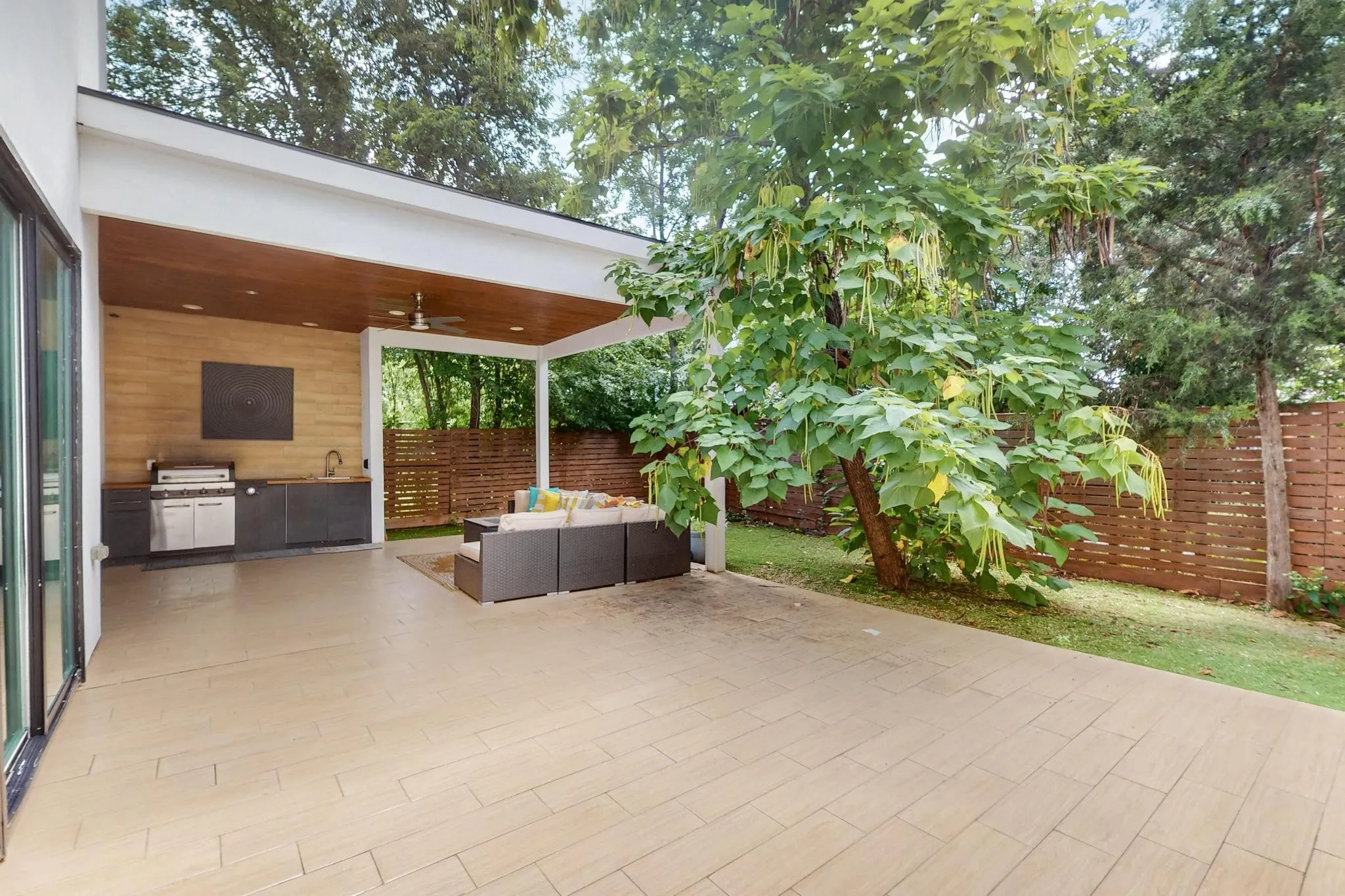 Spacious outdoor patio featuring wood-finish ceiling, built-in outdoor kitchen with grill and sink, ceiling fan, and sliding glass doors