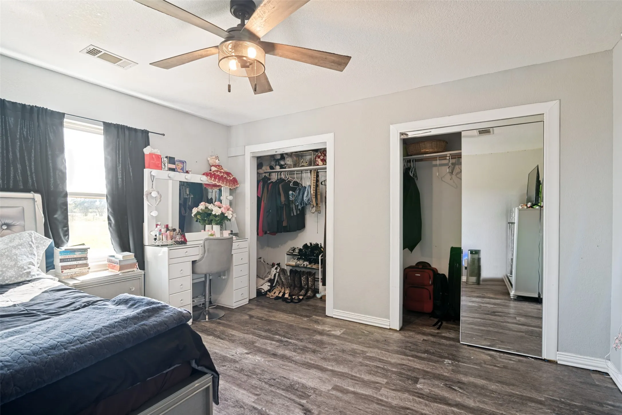 Interior room featuring wood-finish flooring, two closet entries, a window, and a ceiling fan with integrated lighting