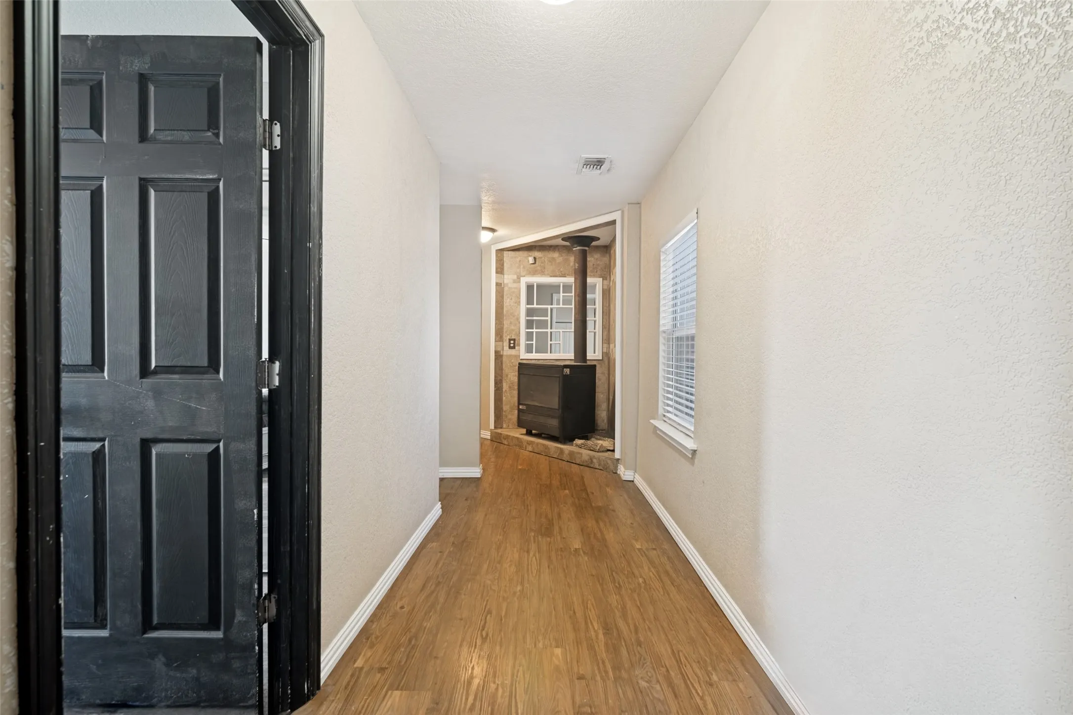 Corridor featuring wood-finish flooring, light-toned textured walls, and a window with horizontal blinds