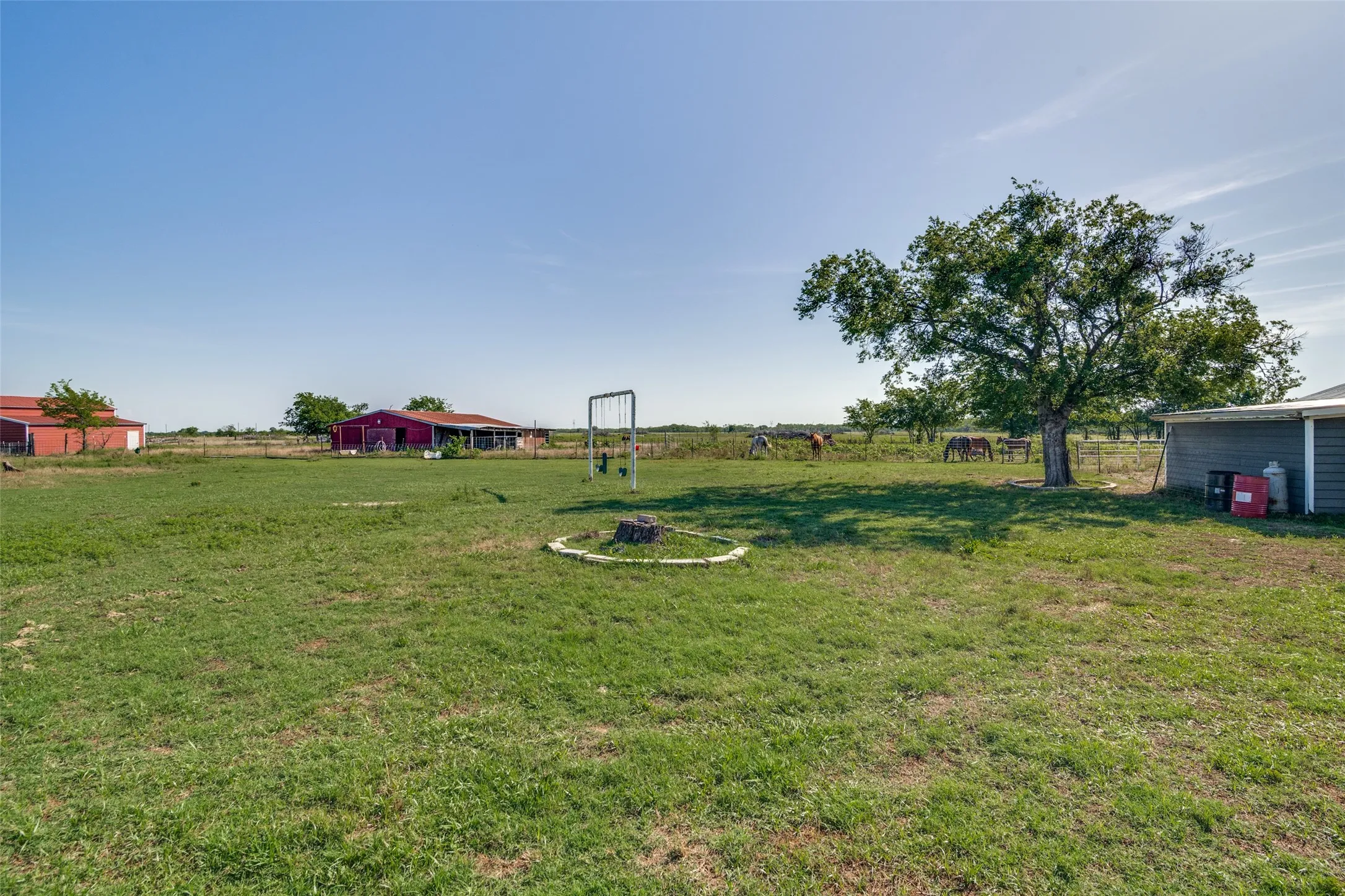 Expansive grassy acreage featuring mature trees, multiple red barn structures, a grey outbuilding, and fencing