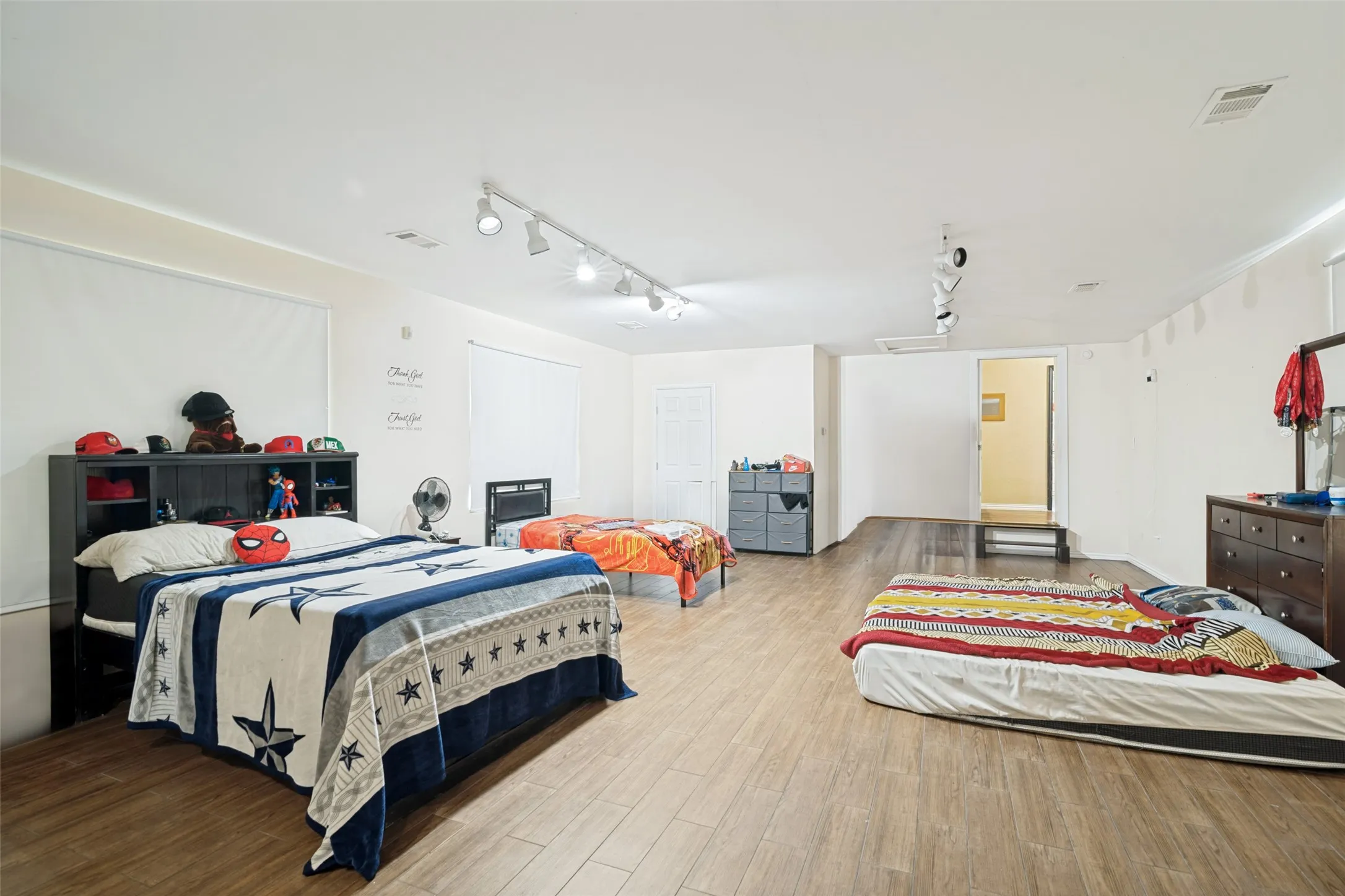 Spacious room featuring wood-finish flooring, white walls, and track lighting