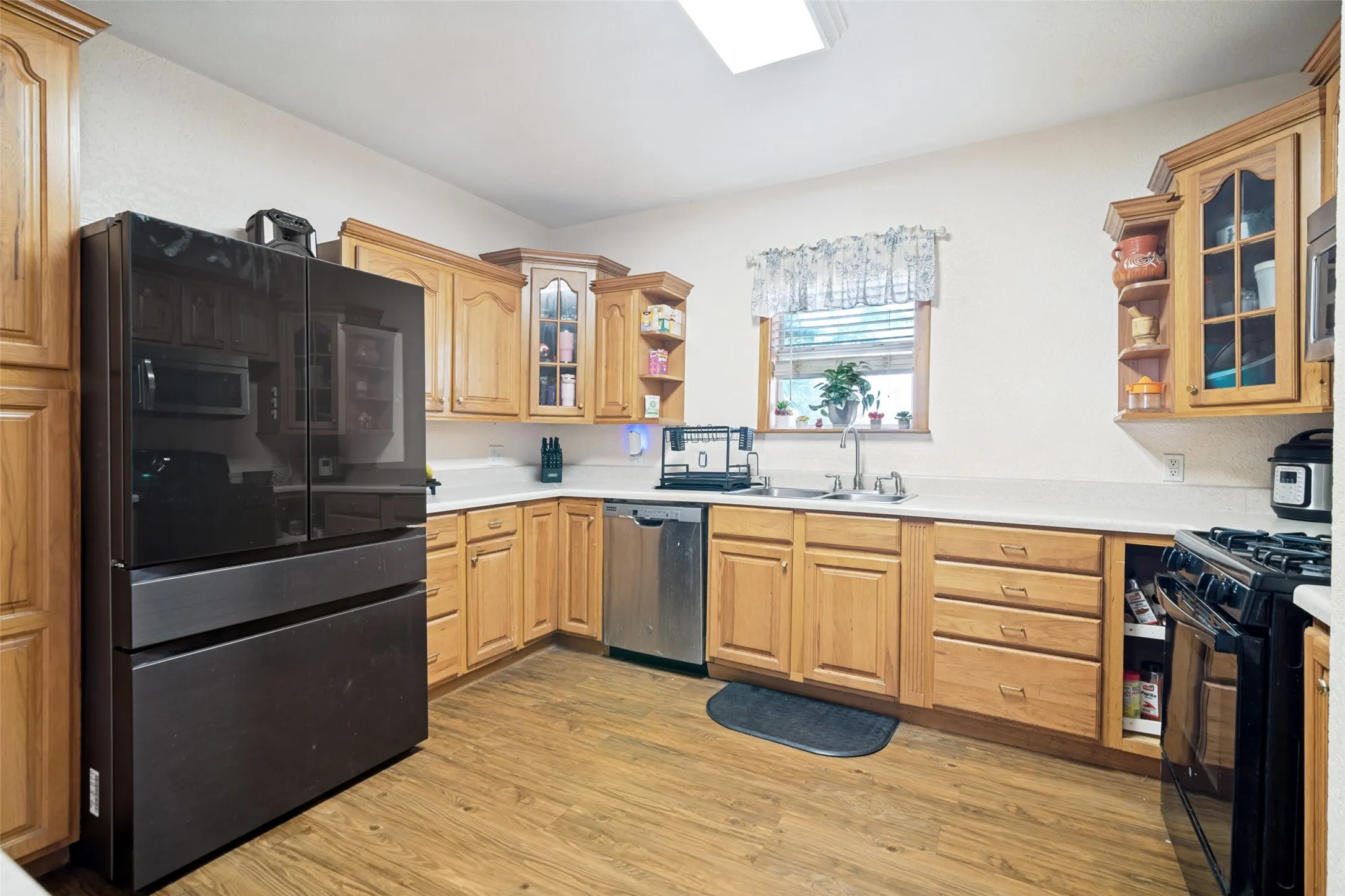 Kitchen featuring wood-finish flooring, light wood cabinetry, white countertops, a black built-in refrigerator, and a stainless steel dishwasher