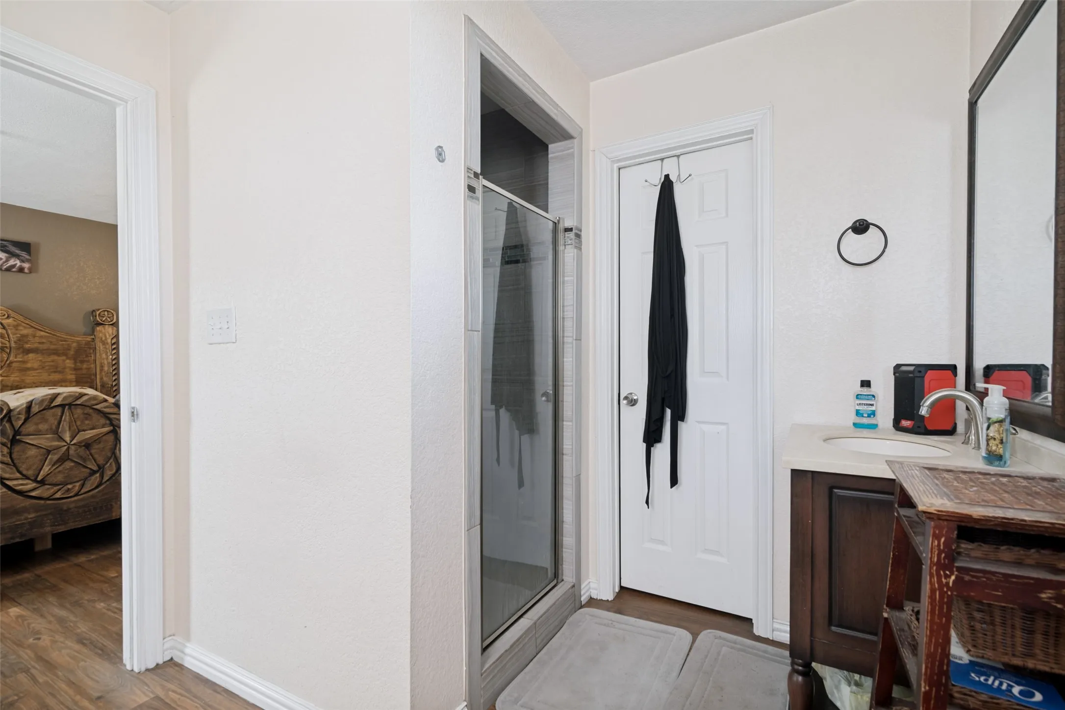 Bathroom featuring a glass-enclosed shower, single vanity with wood-finish cabinetry and a light-toned countertop, and wood-finish flooring