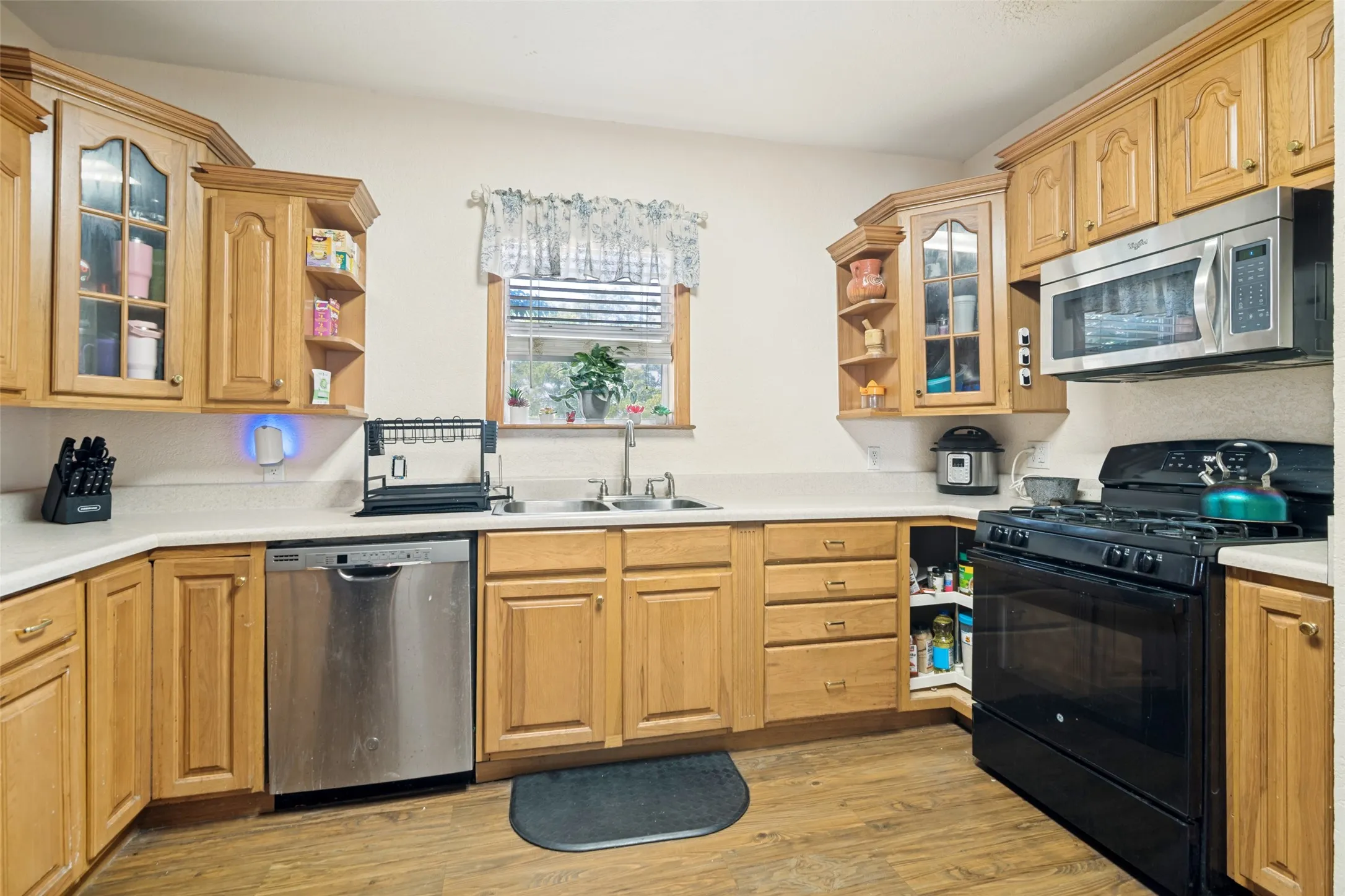 Kitchen featuring wood-finish cabinetry, light-toned countertops, a stainless steel dishwasher, a black gas range, and an over-the-range microwave