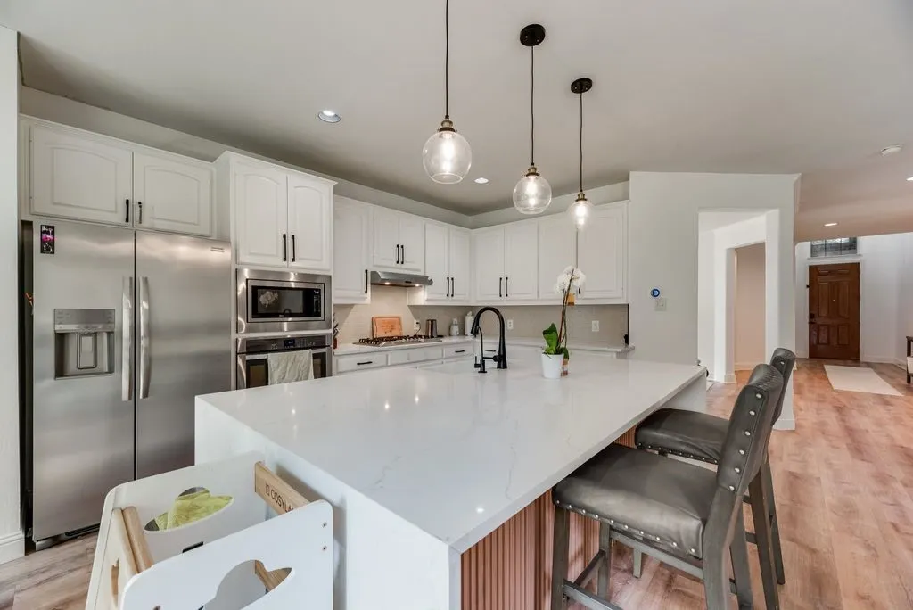 Kitchen featuring white cabinetry, stainless steel appliances, a large center island with a waterfall edge, and wood-finish flooring