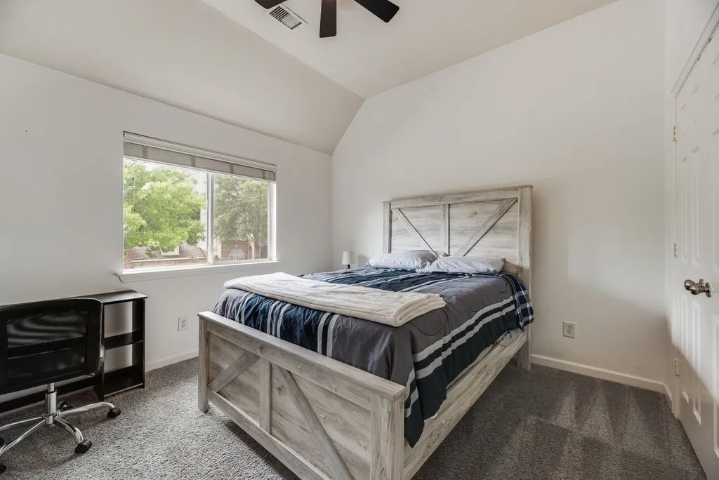 Vaulted ceiling room featuring a large window, neutral carpeting, and a ceiling fan with integrated lighting