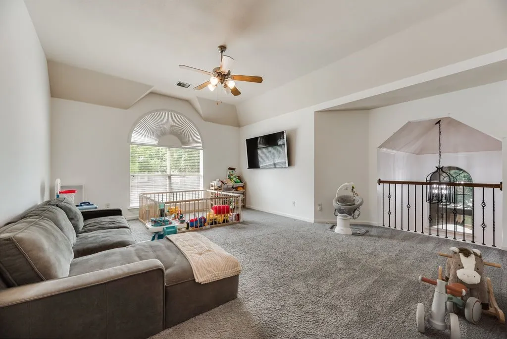 Carpeted room featuring a large arched window, vaulted ceiling, and a ceiling fan with light fixture