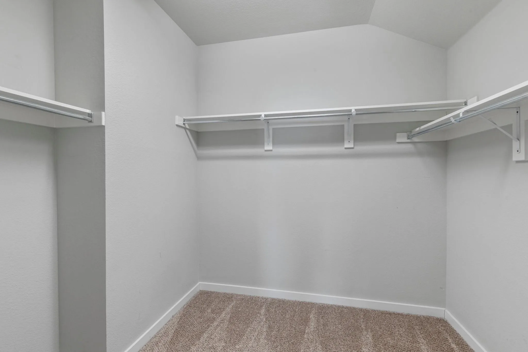 Walk-in closet featuring white wire shelving and hanging rods, light gray walls, white baseboards, and neutral-toned carpet flooring