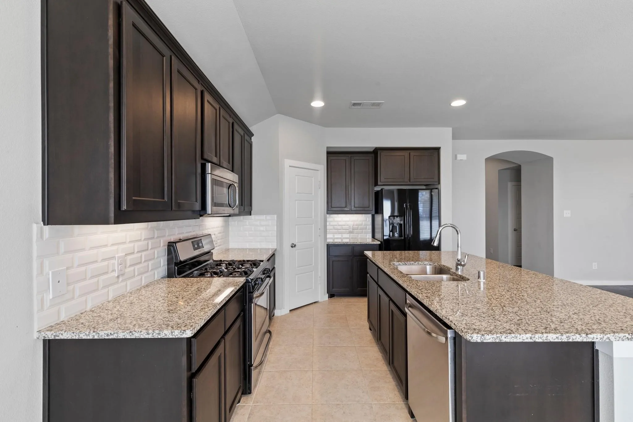 Modern kitchen featuring dark wood cabinetry, light speckled countertops, and a white subway tile backsplash