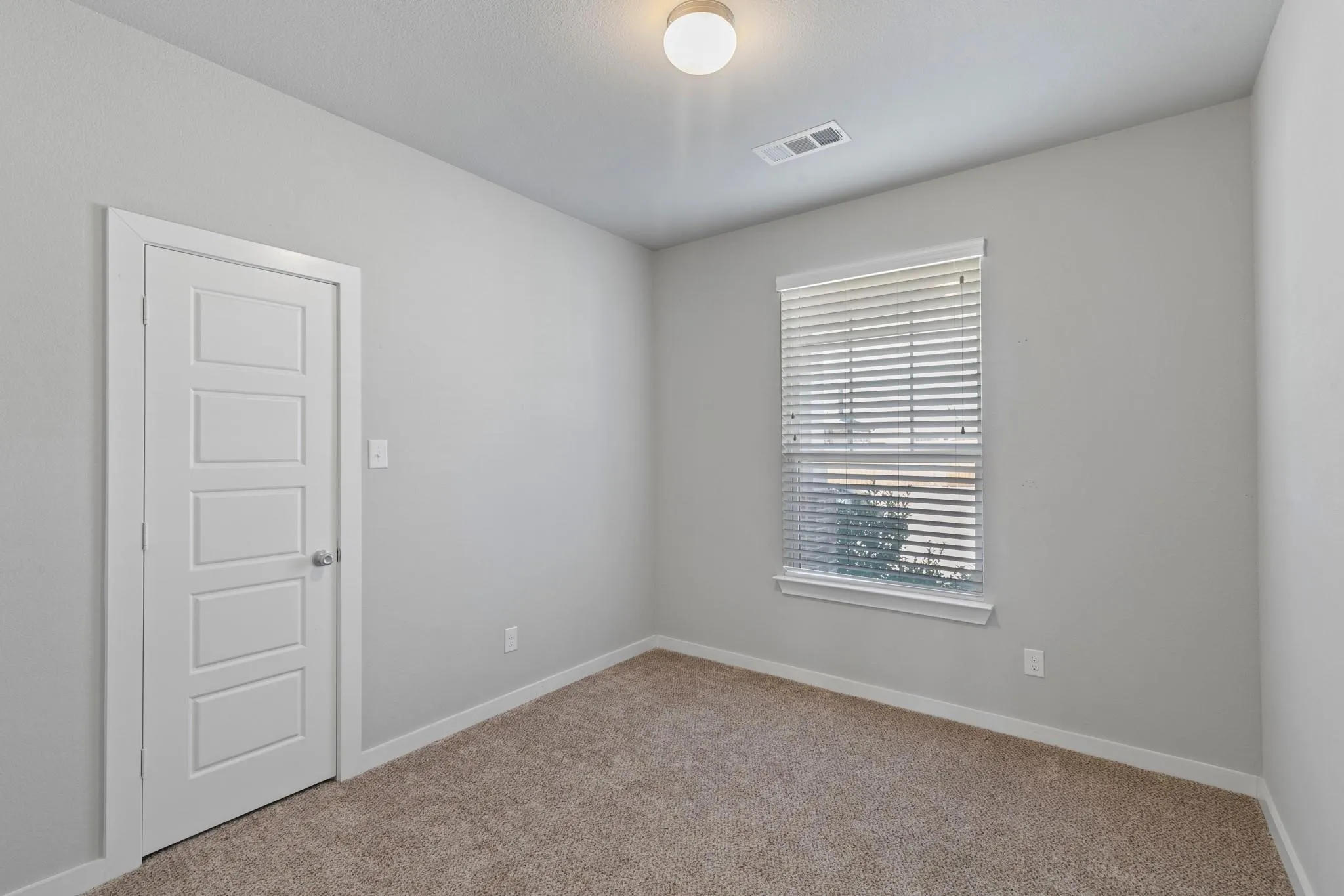 Neutral-toned room featuring a single window with horizontal blinds, light gray walls, and textured carpeting