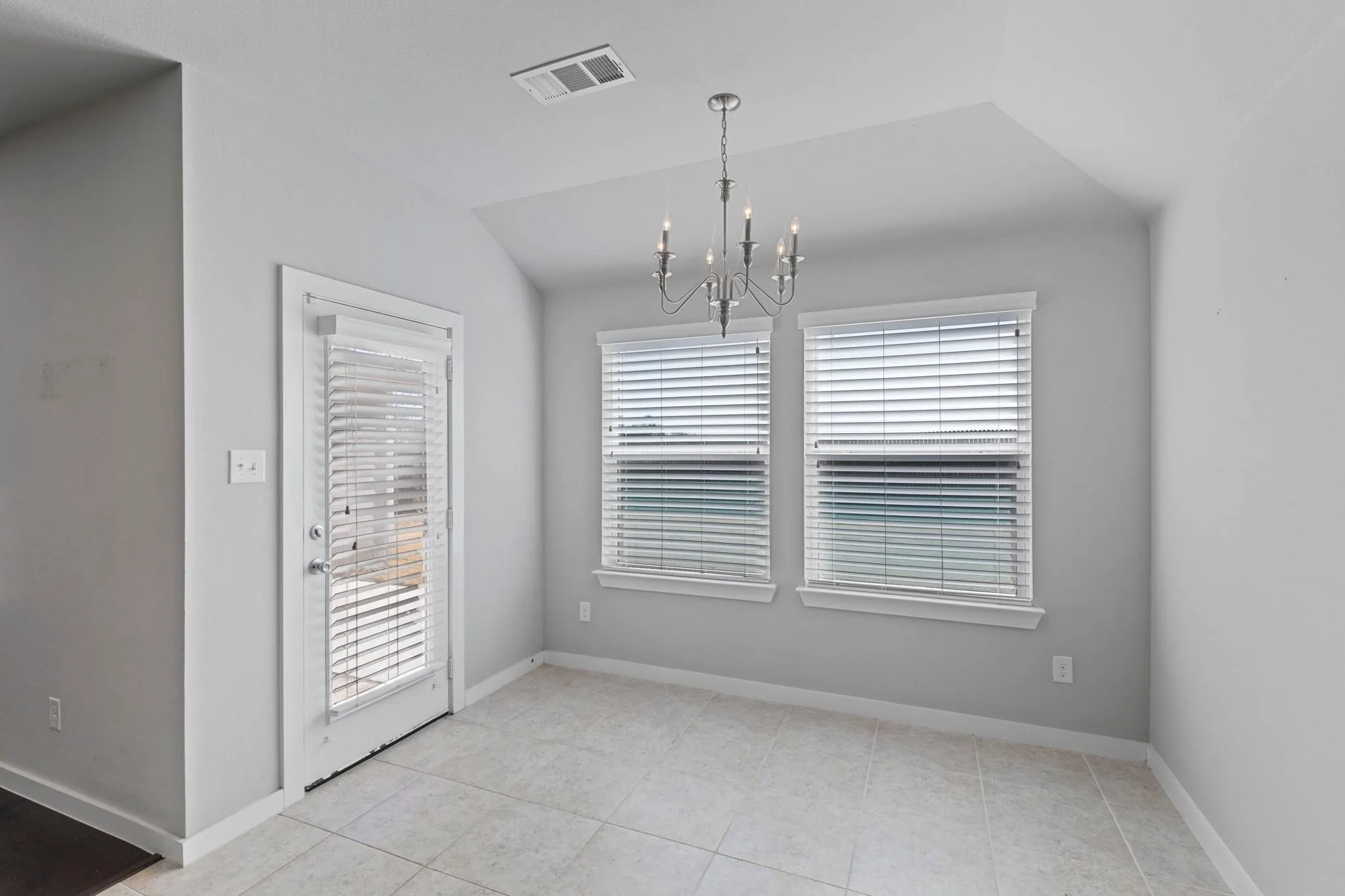 Dining area featuring a modern chandelier, two windows with blinds, a glass-paned door, light-toned tile flooring, and a tray ceiling detail
