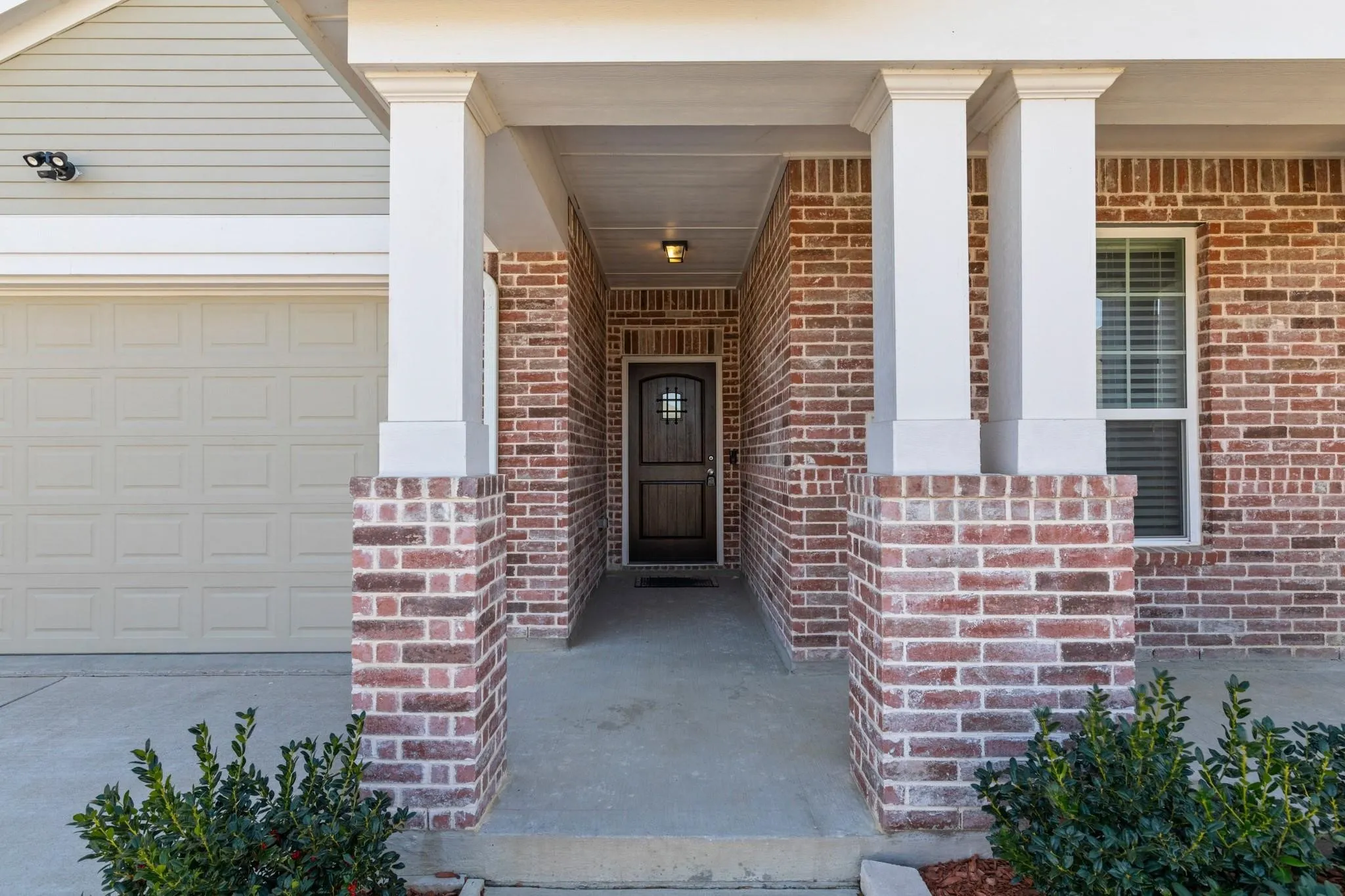 Brick facade with a covered entry, featuring white columns and a concrete porch