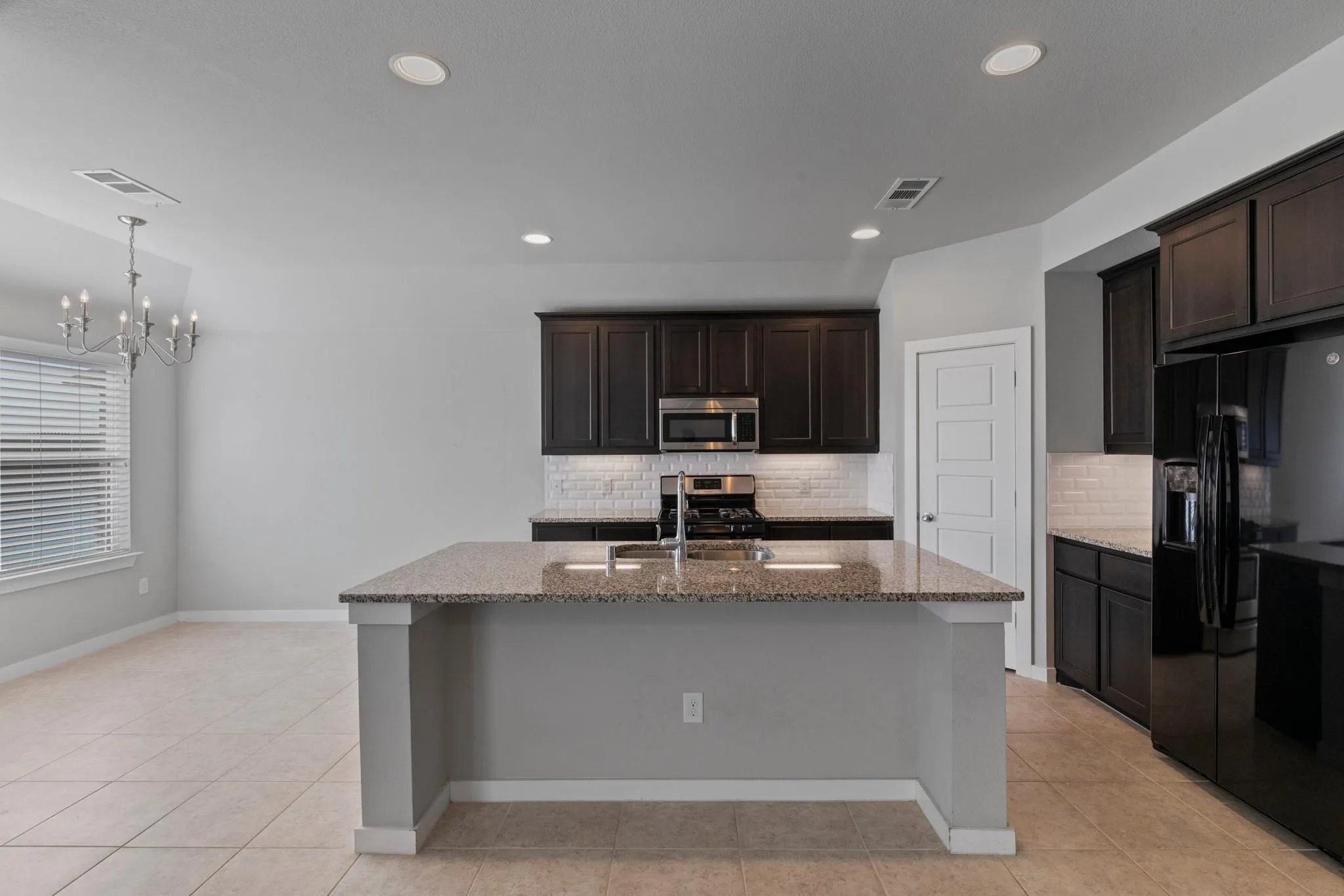 Kitchen featuring a large island with a stone-finish countertop, dark wood-finish cabinetry, subway tile backsplash, and stainless steel appliances