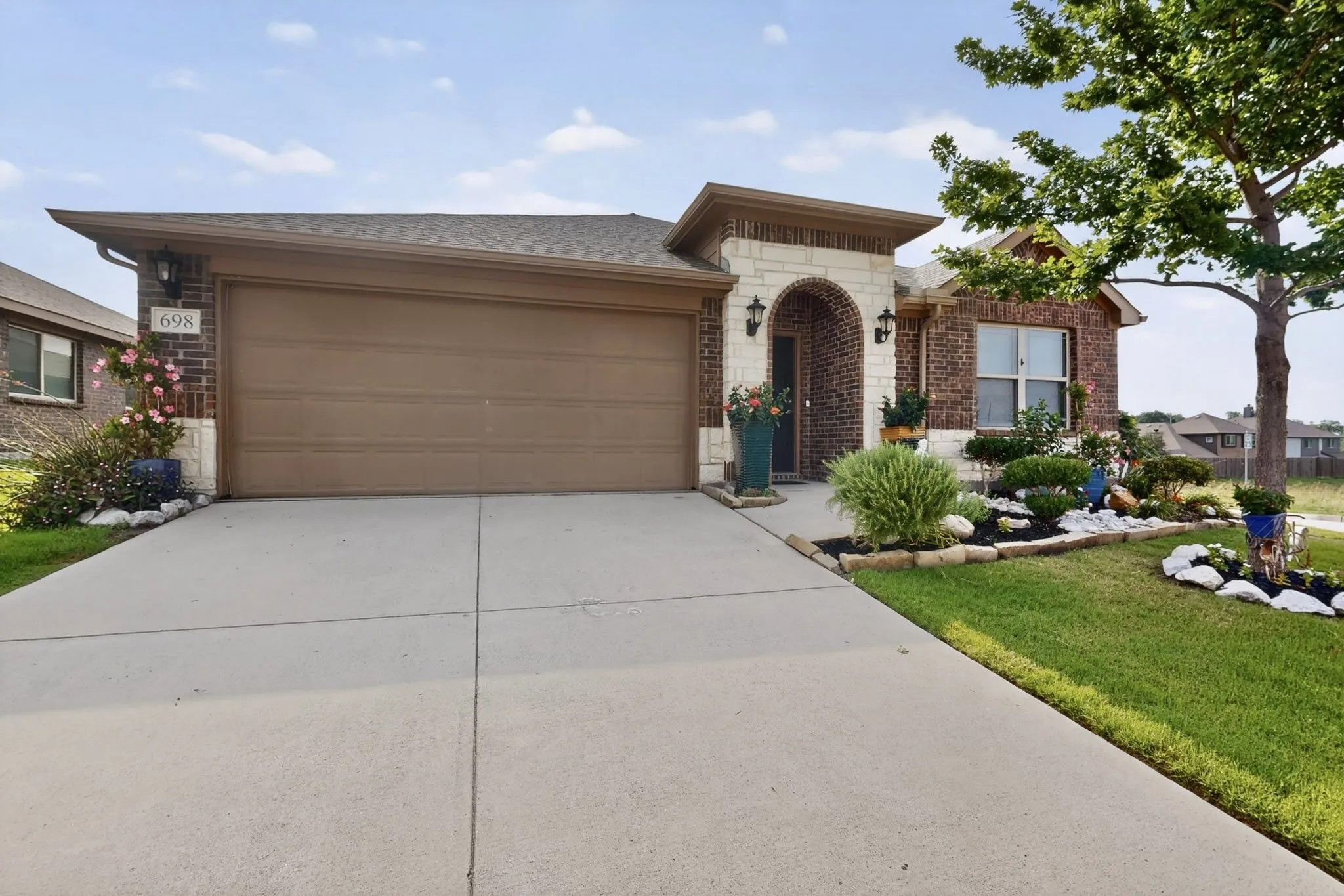 Brick and stone facade featuring an arched entry, a two-car garage, concrete driveway, and established front yard landscaping