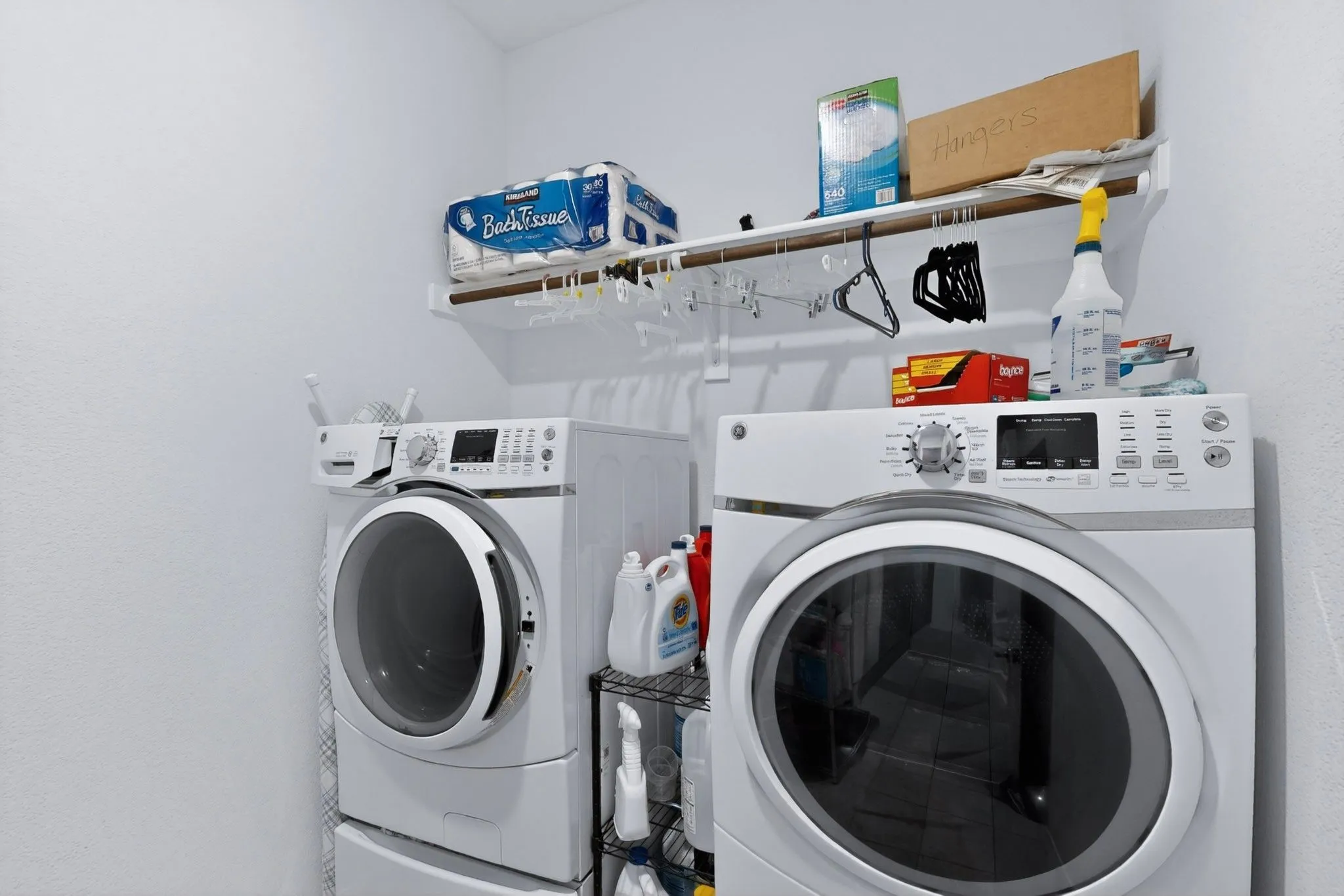 Dedicated laundry area featuring a white front-loading washer and dryer set, a high-mounted storage shelf, and a hanging rod for convenience