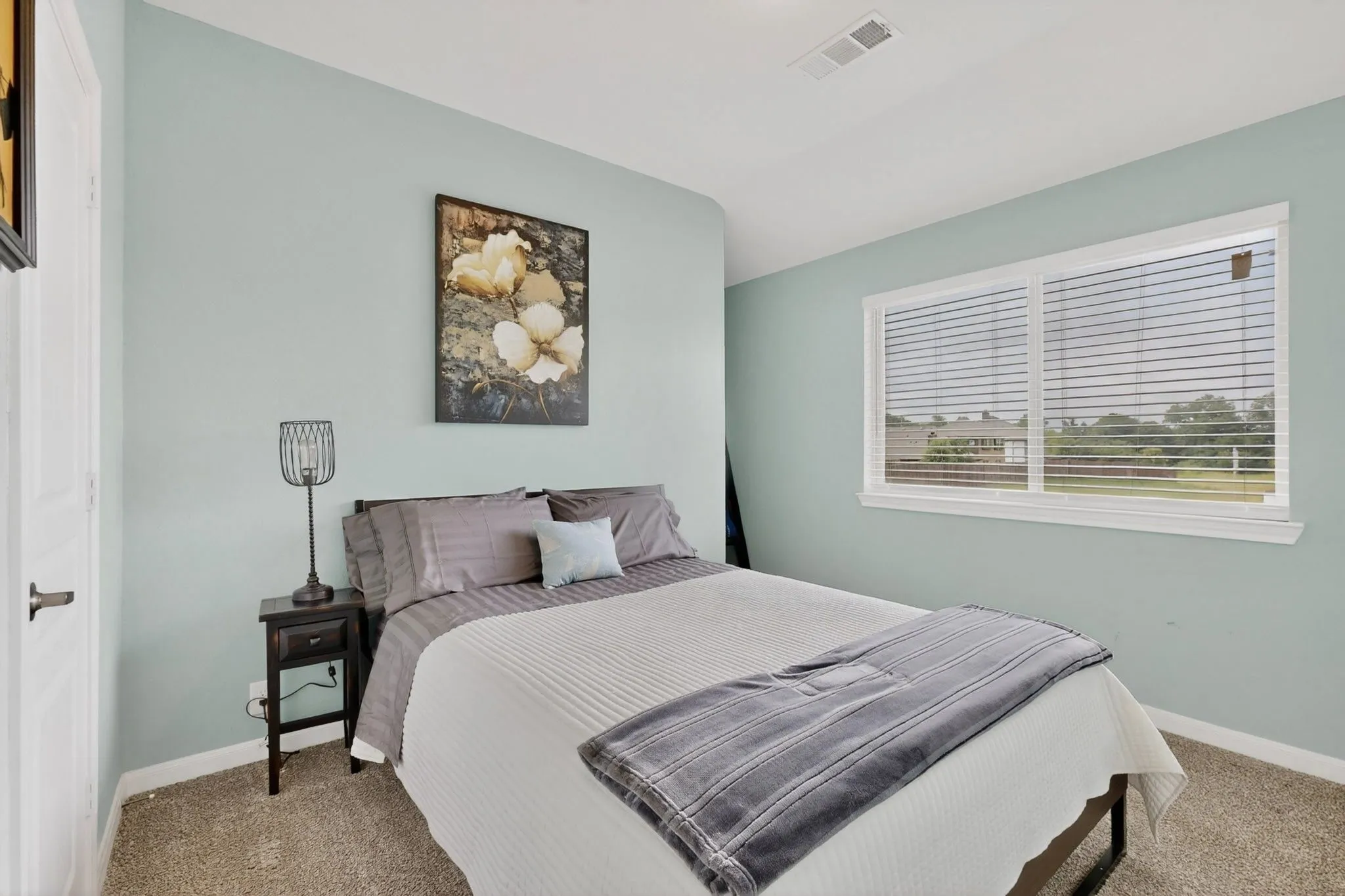 Carpeted room featuring light blue walls, white trim, and a large window with white blinds