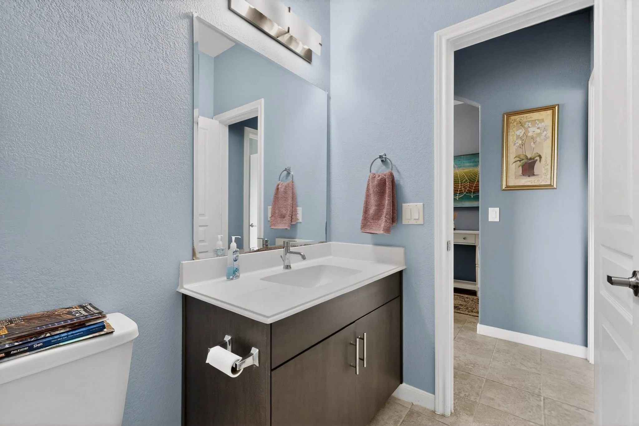 Bathroom vanity featuring a white countertop with integrated sink, dark wood-finish cabinetry, and brushed nickel hardware