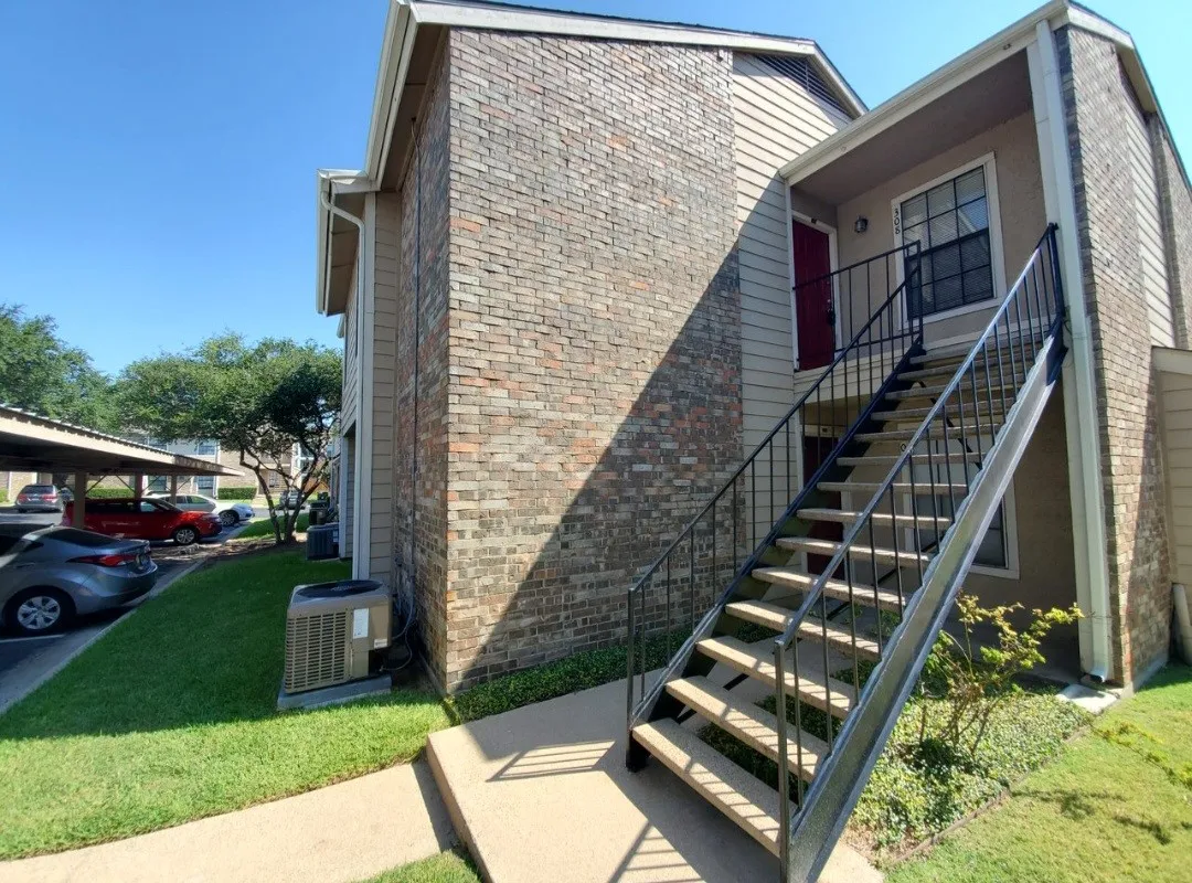 View of home's exterior with brick siding, stairway, cooling unit, and covered parking