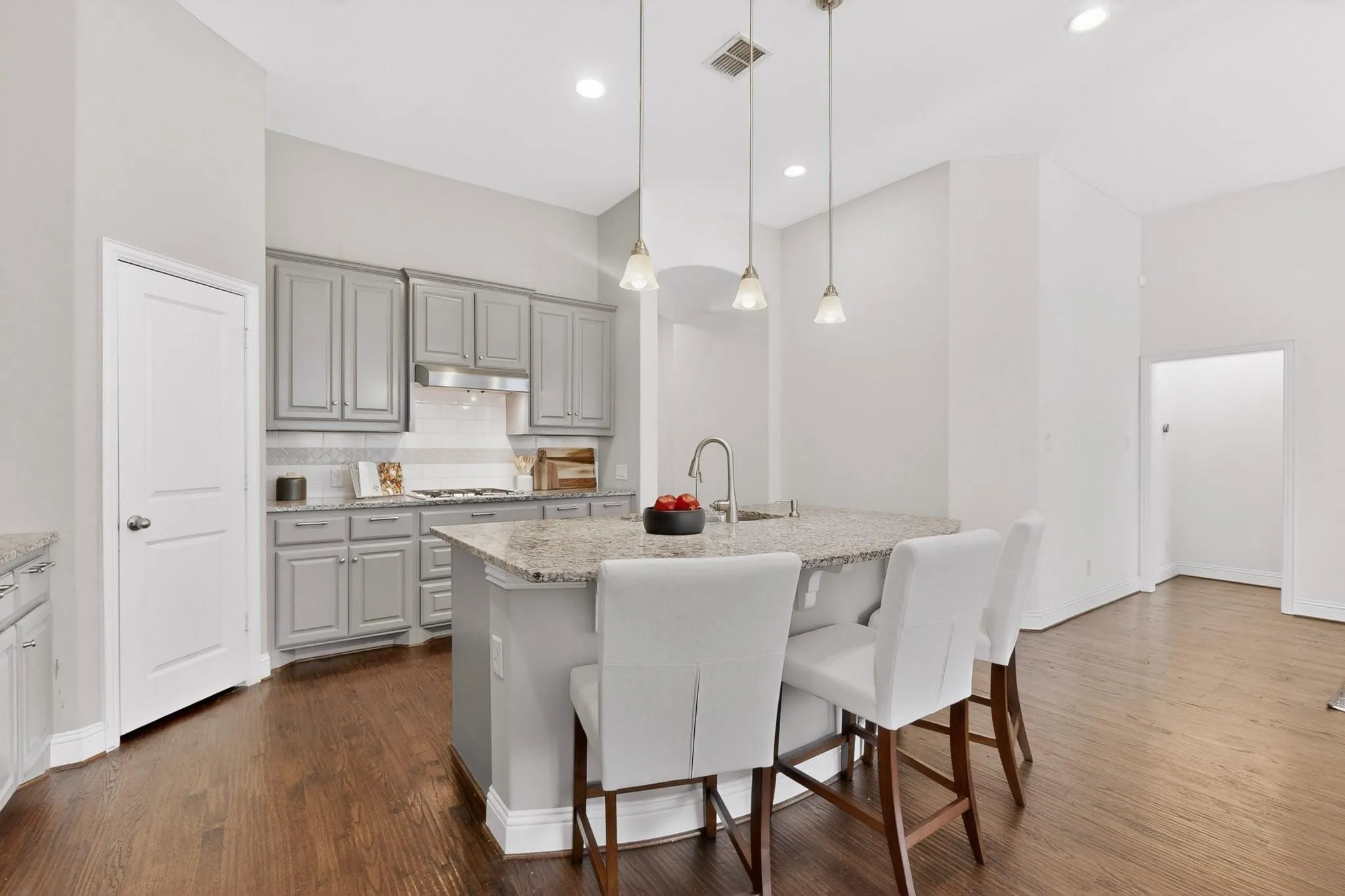 A modern kitchen featuring a kitchen island, stainless steel appliances, warm hardwood floor and decorative lighting, creating a stylish and inviting atmosphere.