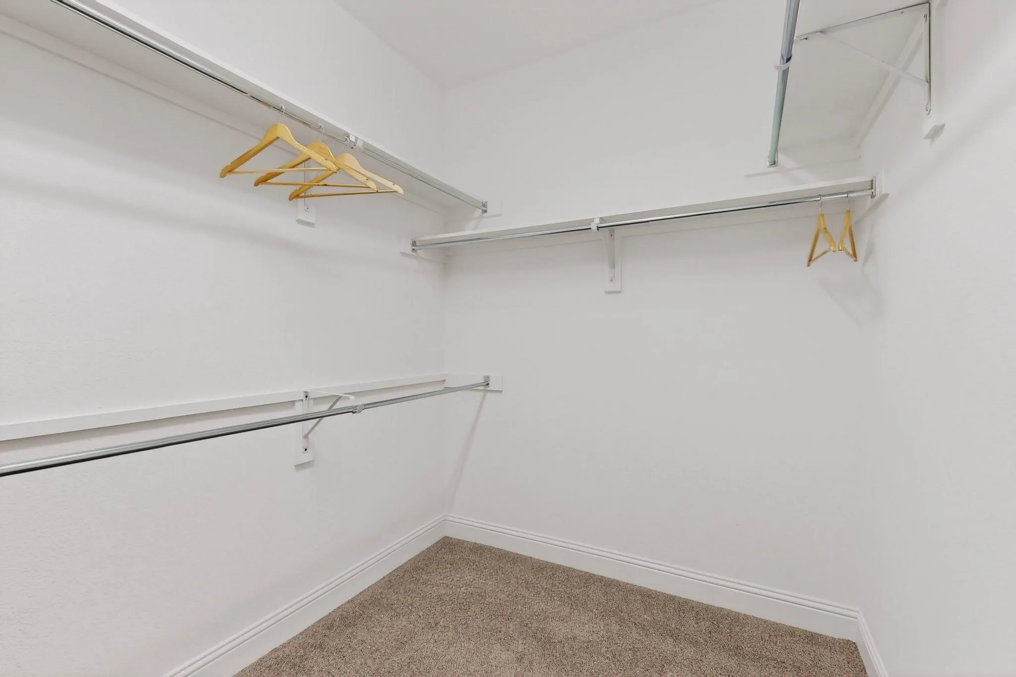 A spacious walk-in closet featuring white walls and neatly arranged shelves