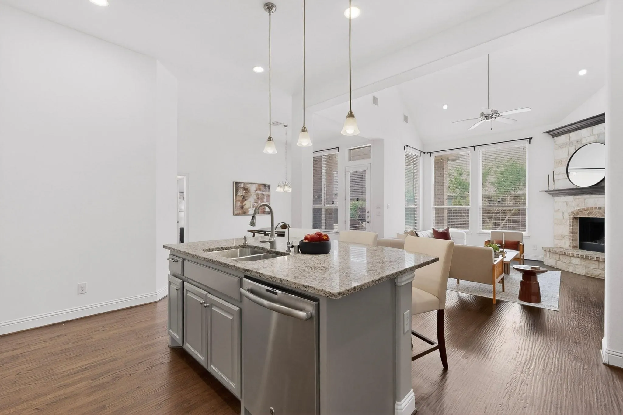 A modern kitchen featuring a kitchen island with dual sink, stainless steel appliances, warm hardwood floor and decorative lighting, creating a stylish and inviting atmosphere.