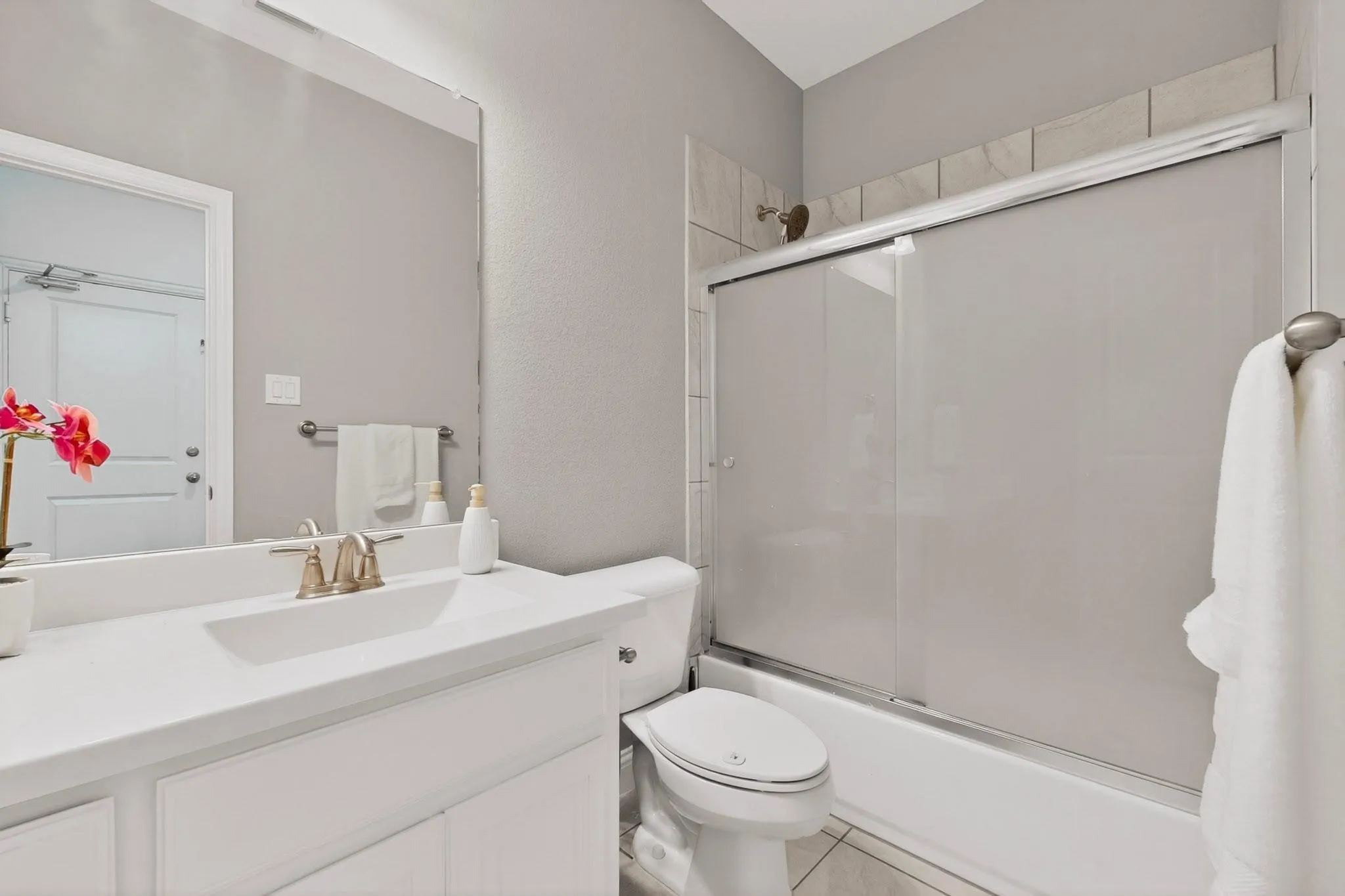 A clean bathroom featuring a shower, toilet, and vanity, with neutral-colored tiles and bright lighting.