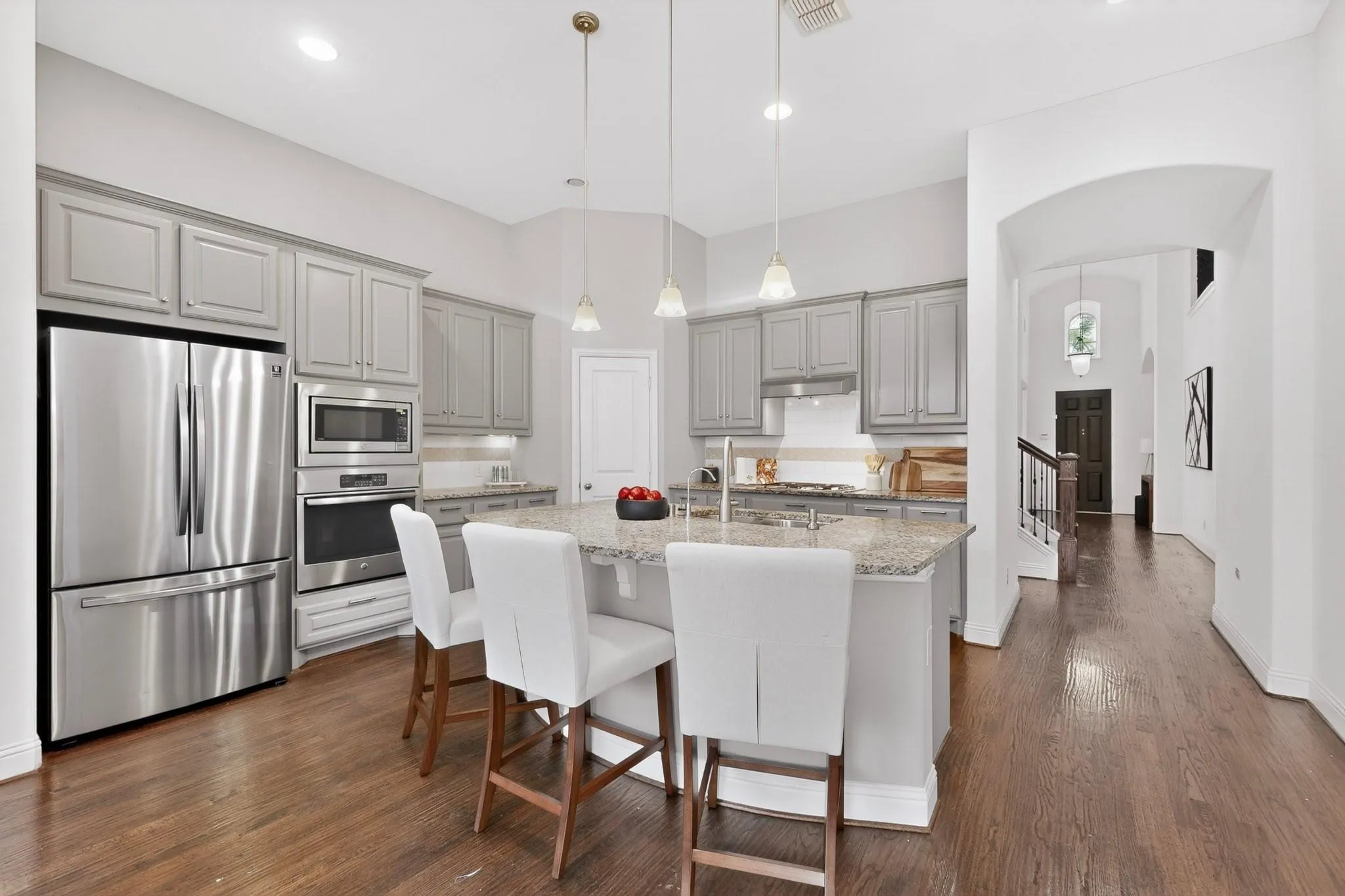 A modern kitchen featuring a kitchen island, stainless steel appliances, warm hardwood floor and decorative lighting, creating a stylish and inviting atmosphere.