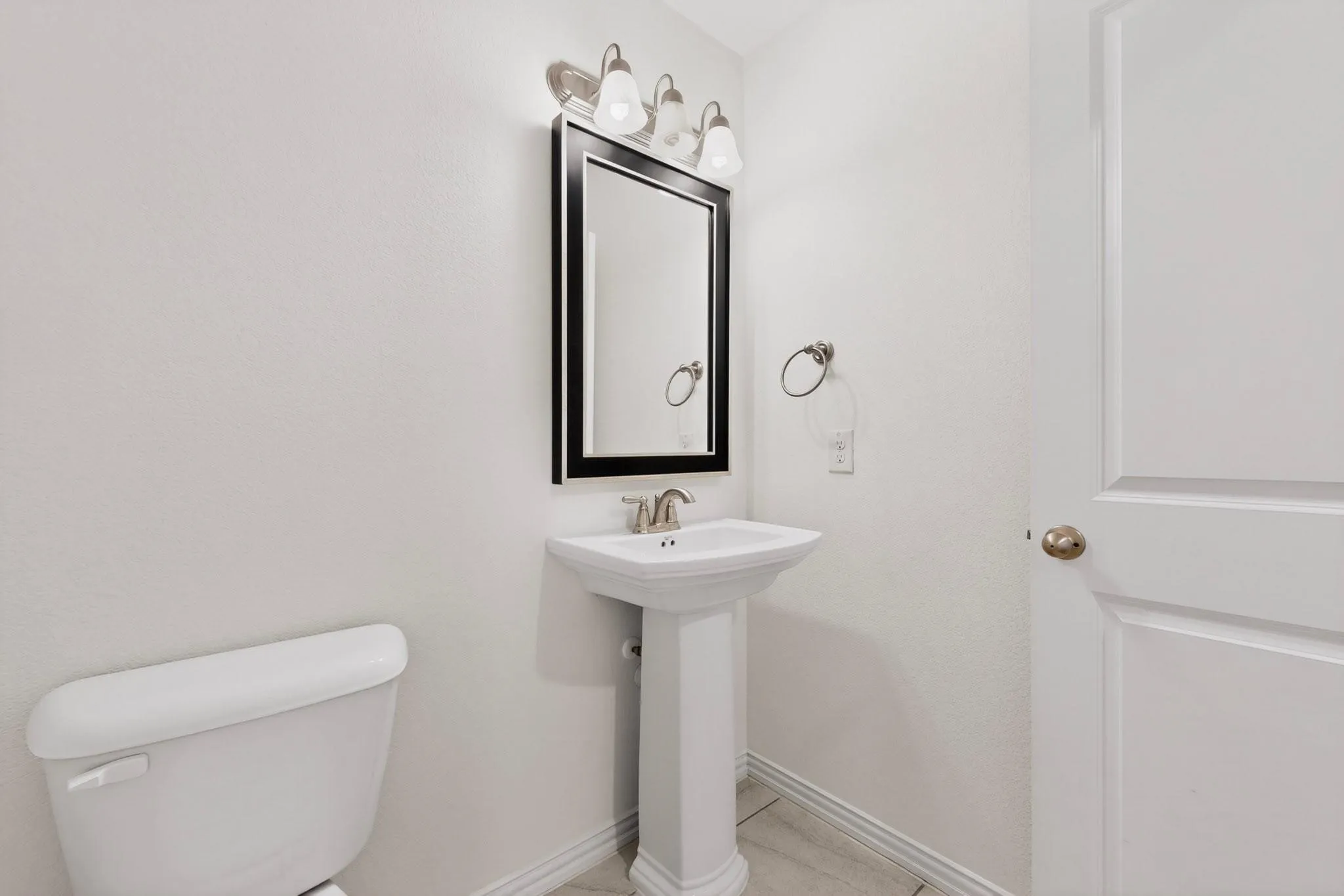 A clean and simple half-bathroom layout showcasing a sink, toilet, and a mirror on the wall.