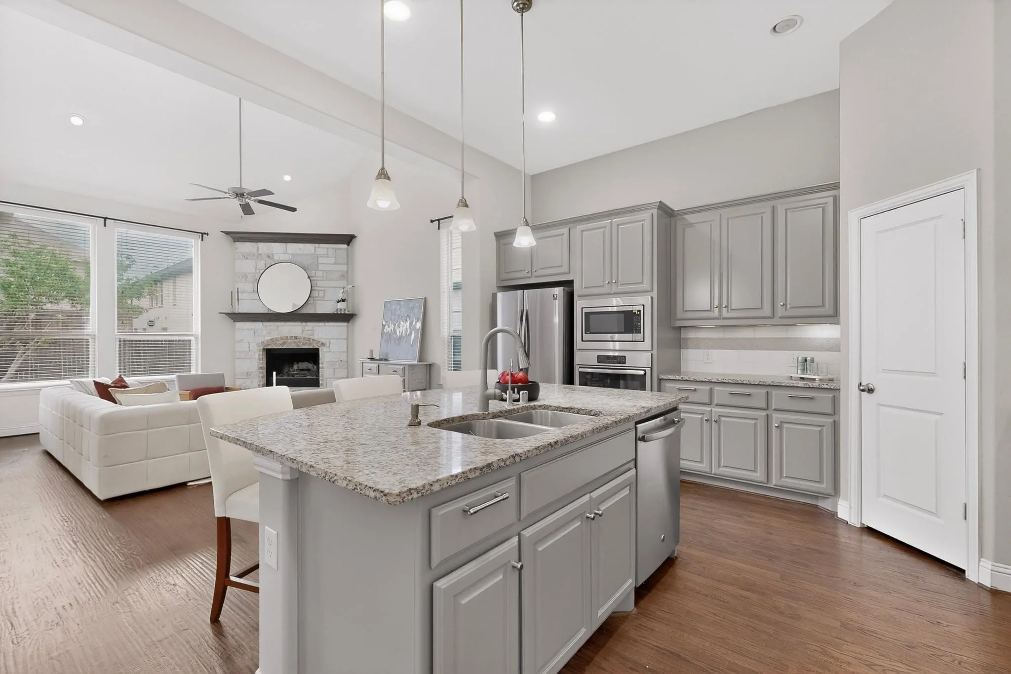 A modern kitchen featuring a kitchen island with dual sink, stainless steel appliances, warm hardwood floor and decorative lighting, creating a stylish and inviting atmosphere.